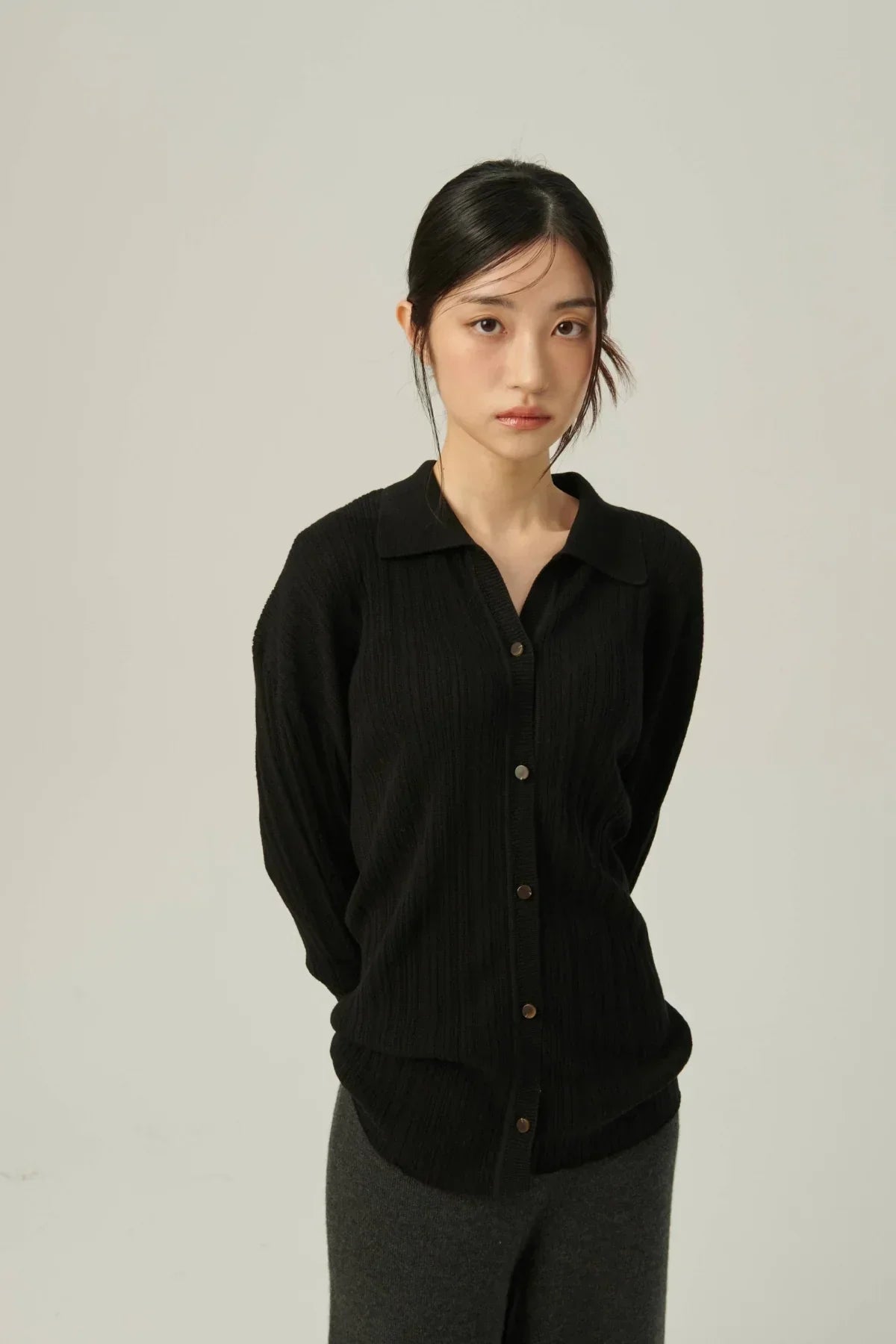 Asian woman wearing black collared rib-knit cardigan with buttons and dark gray pants on neutral background