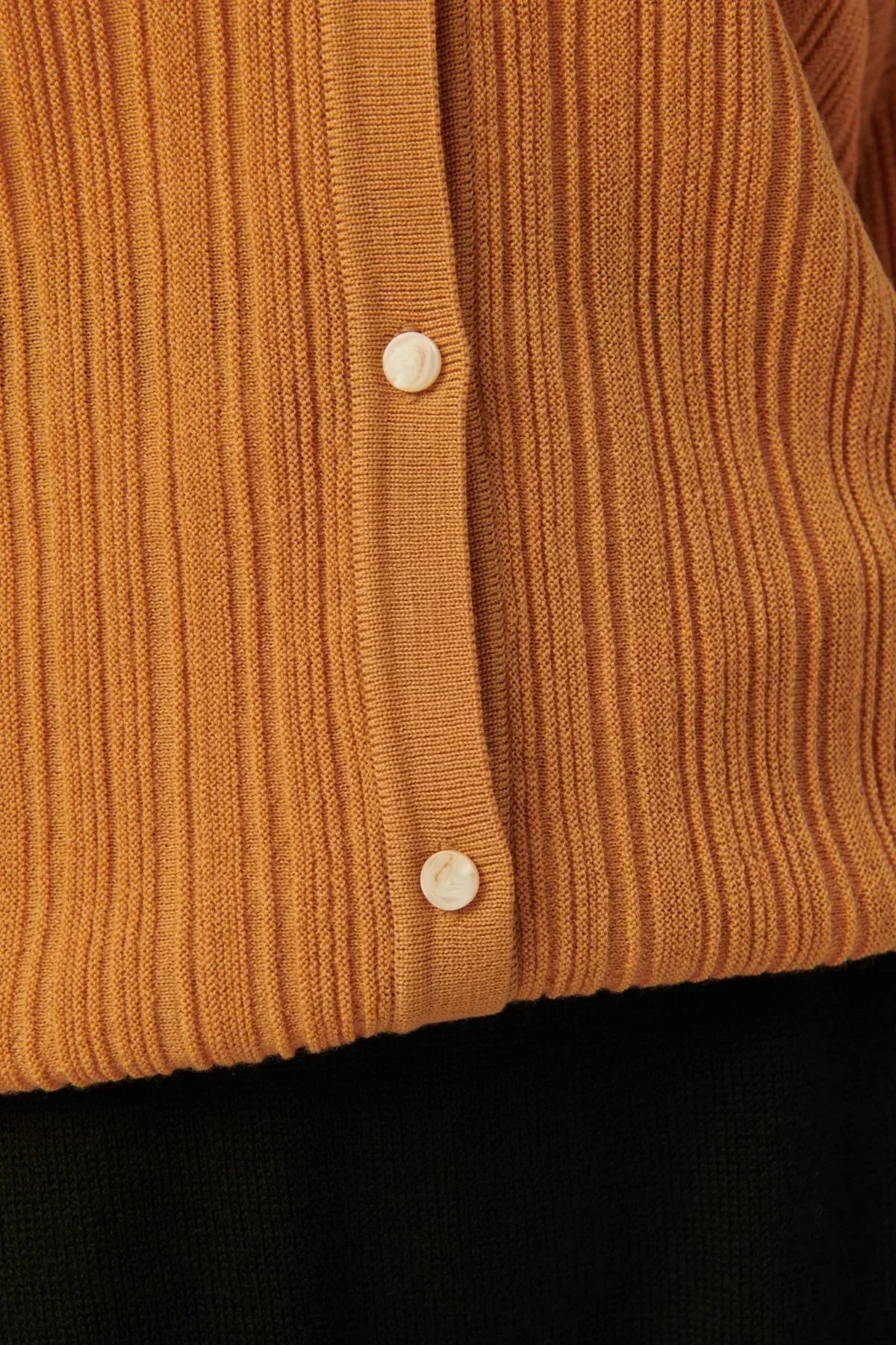 Close-up of camel rib-knit cardigan with cream buttons over black fabric