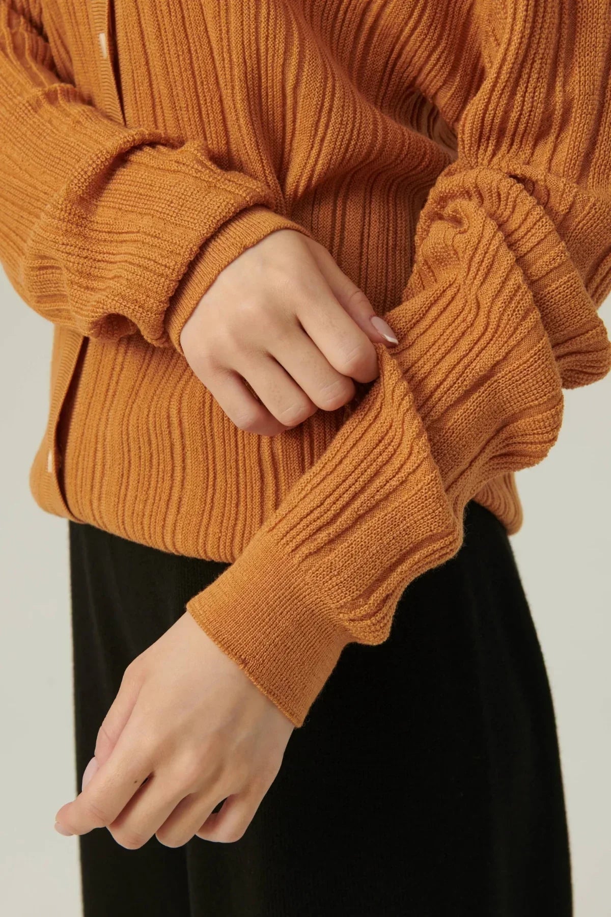 Close-up of hands adjusting camel-colored rib knit cardigan with button details
