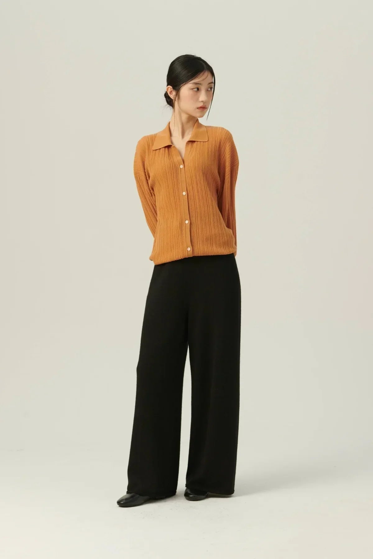 Woman wearing a camel rib-knit buttoned cardigan with wide black pants and black shoes on plain background