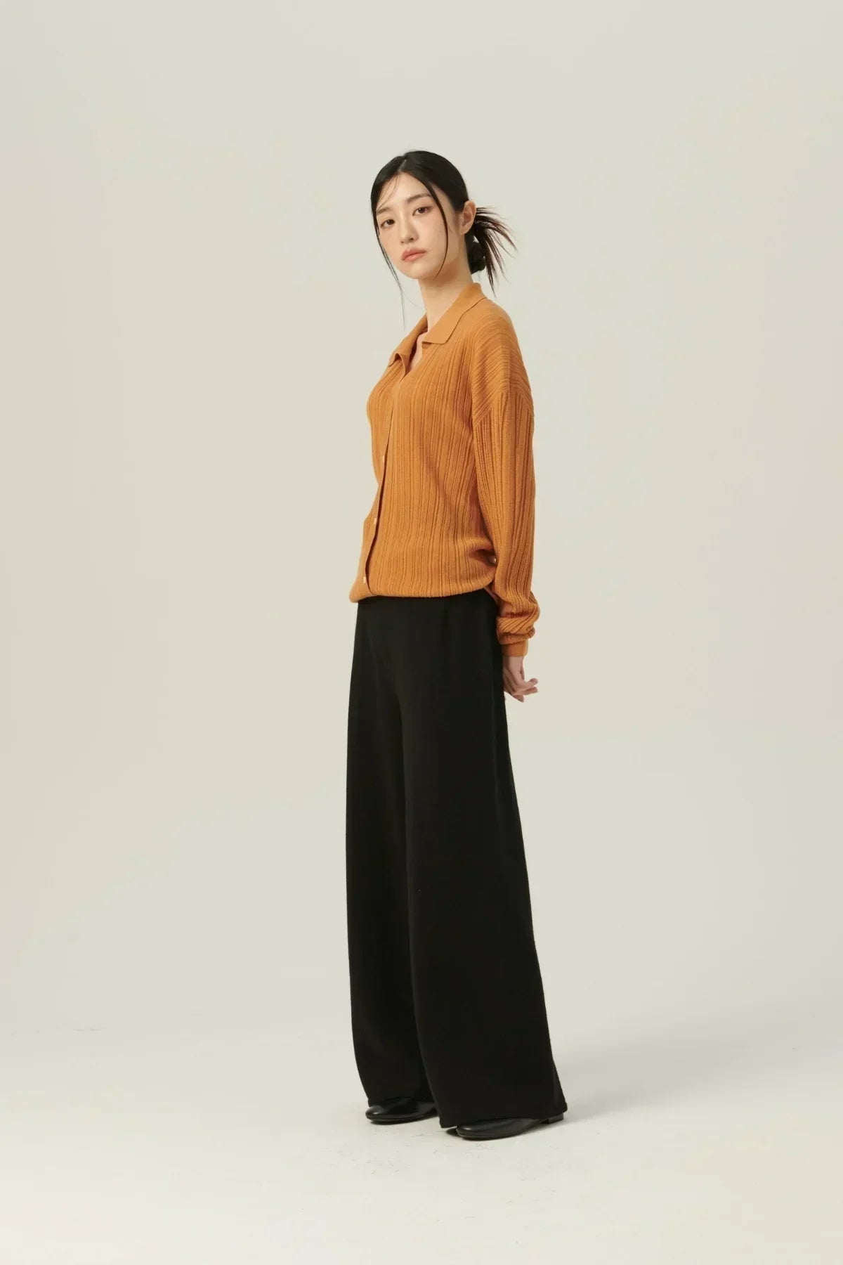Asian woman wearing camel rib knit collared cardigan with black wide-leg pants on beige background