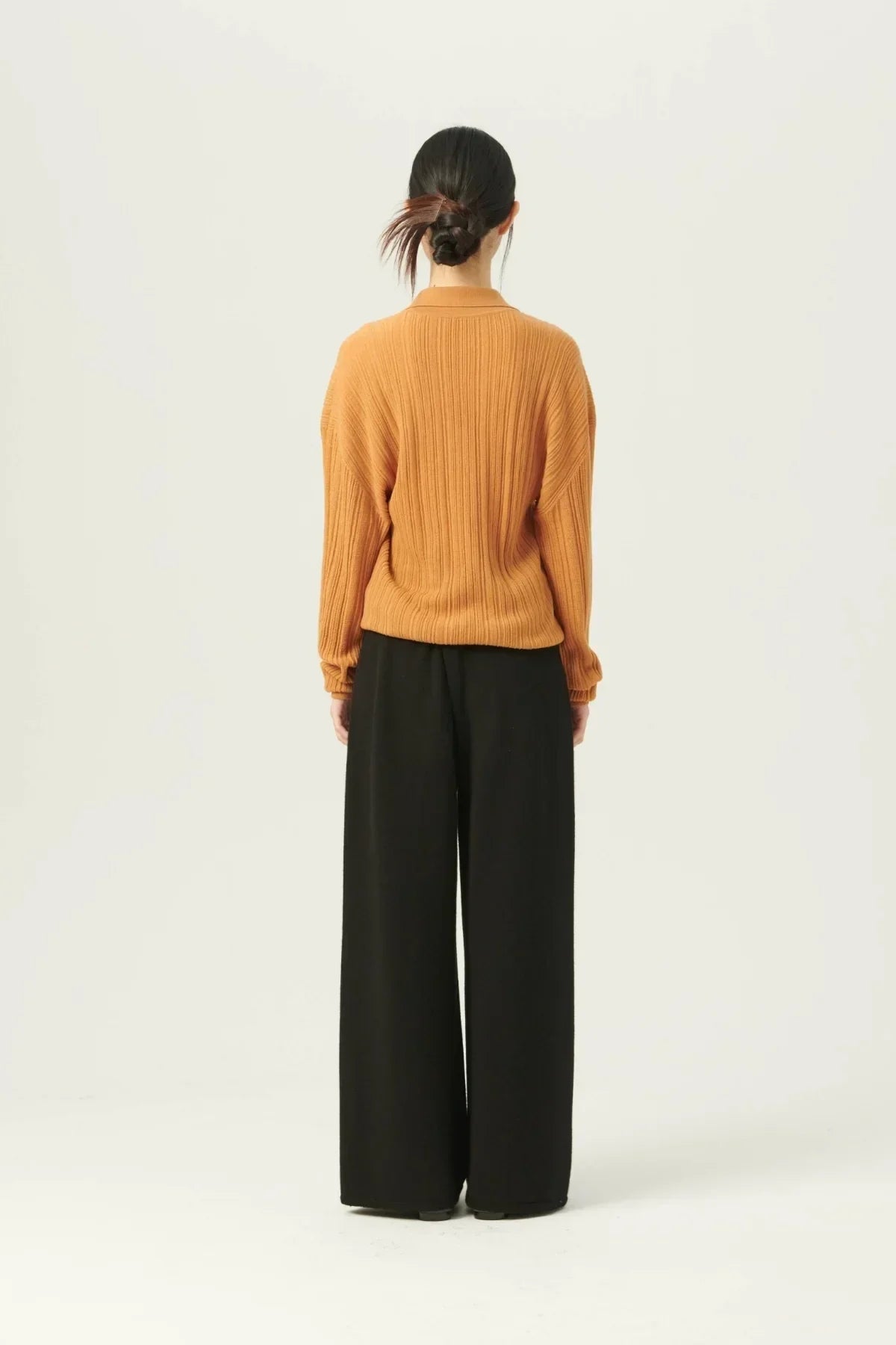 Back view of woman wearing camel rib knit cardigan and black wide-leg pants in studio