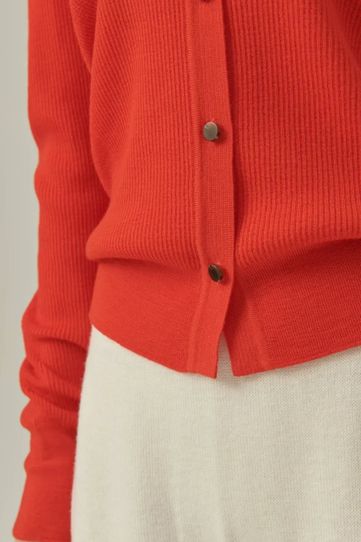 Close-up of red collared rib knit cardigan with buttons paired with white knit bottom