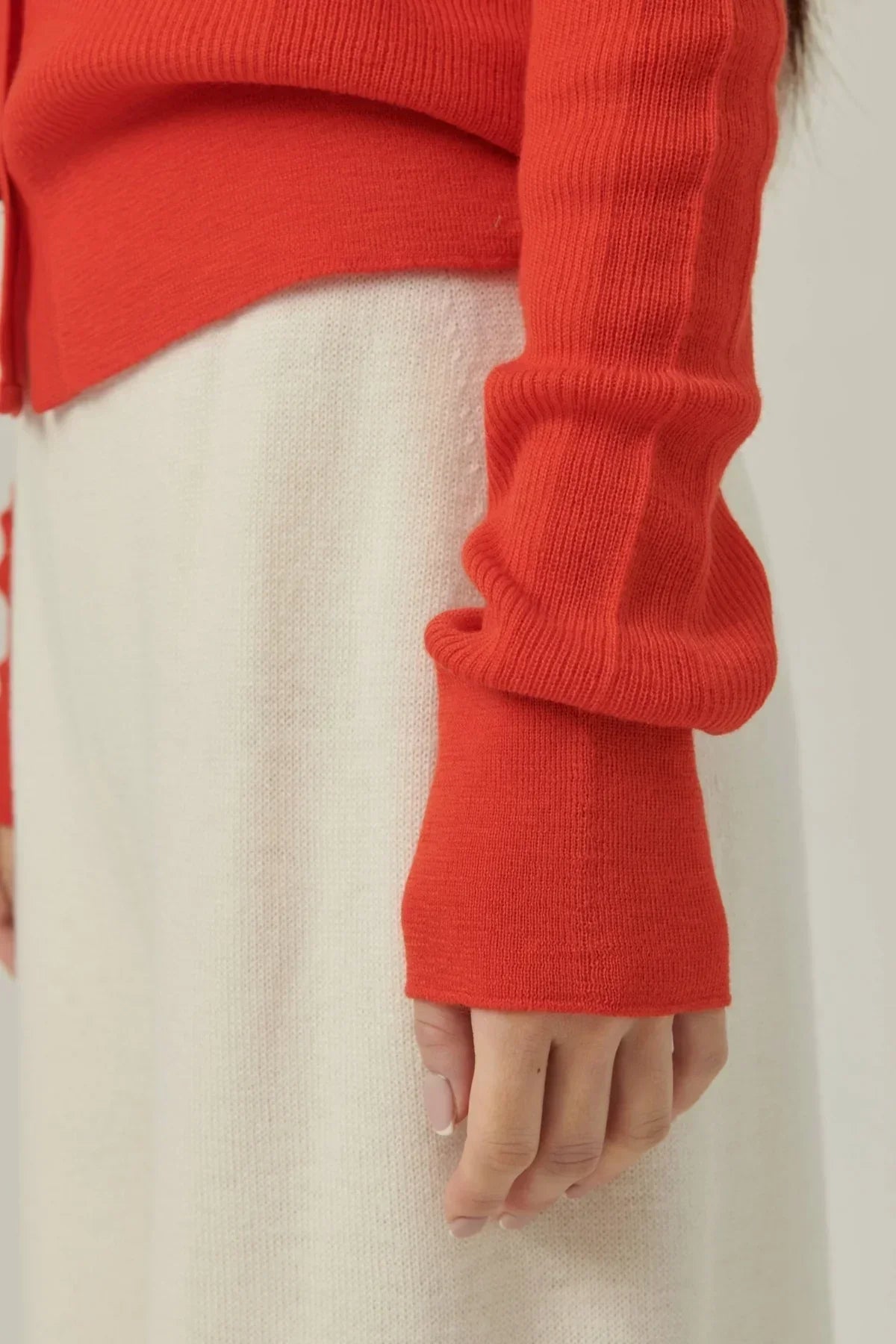 Close-up of a hand wearing a red rib knit cardigan sleeve over a white knit skirt