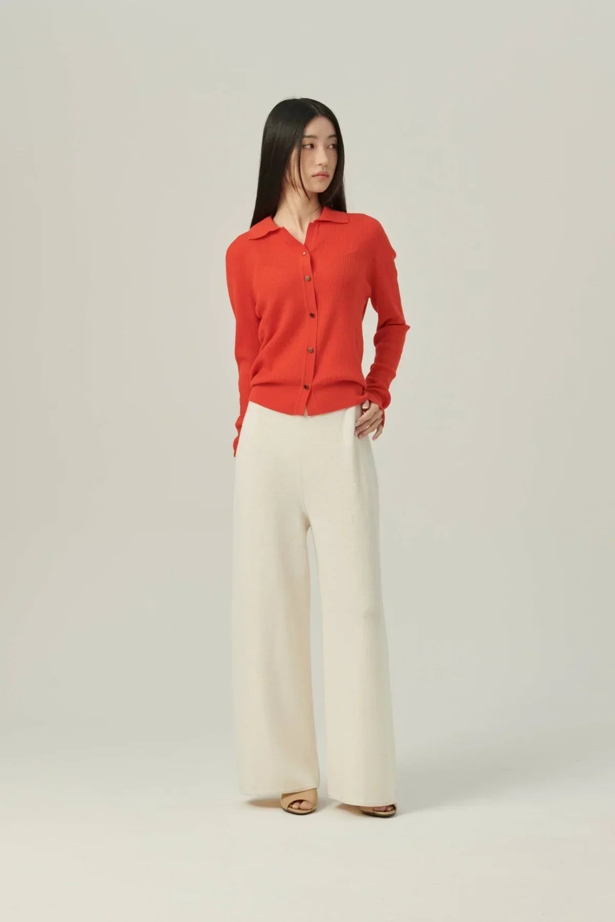 Woman wearing red collared rib knit cardigan and cream wide-leg pants against plain background