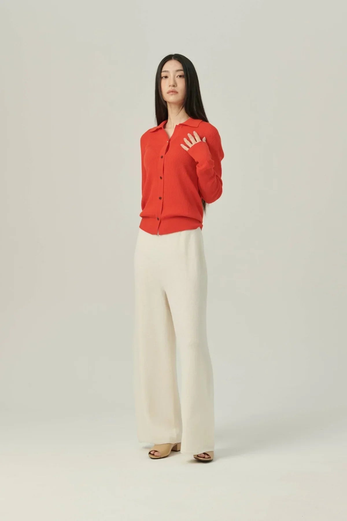 Woman wearing a red collared rib knit cardigan with white wide-leg pants and beige open-toe heels