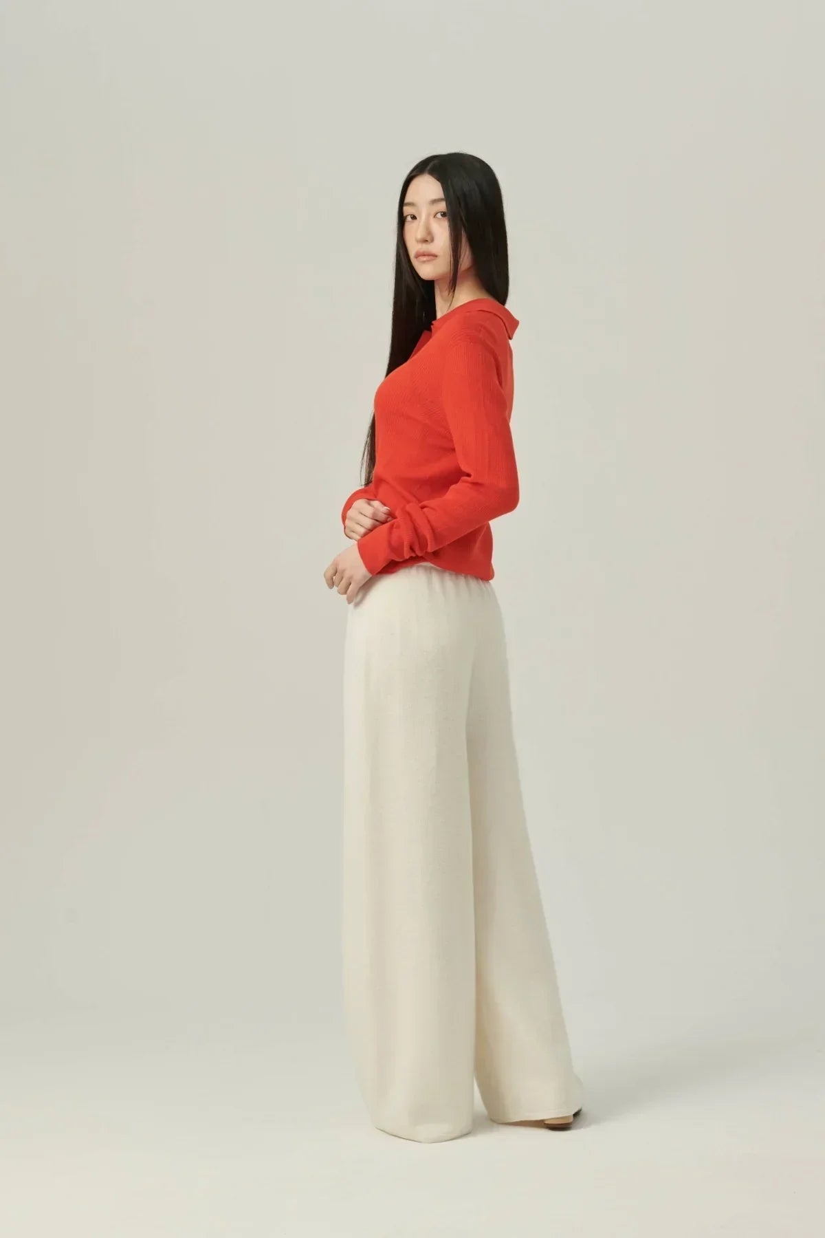 Model wearing a red collared rib knit cardigan and white wide-leg knit pants on beige background