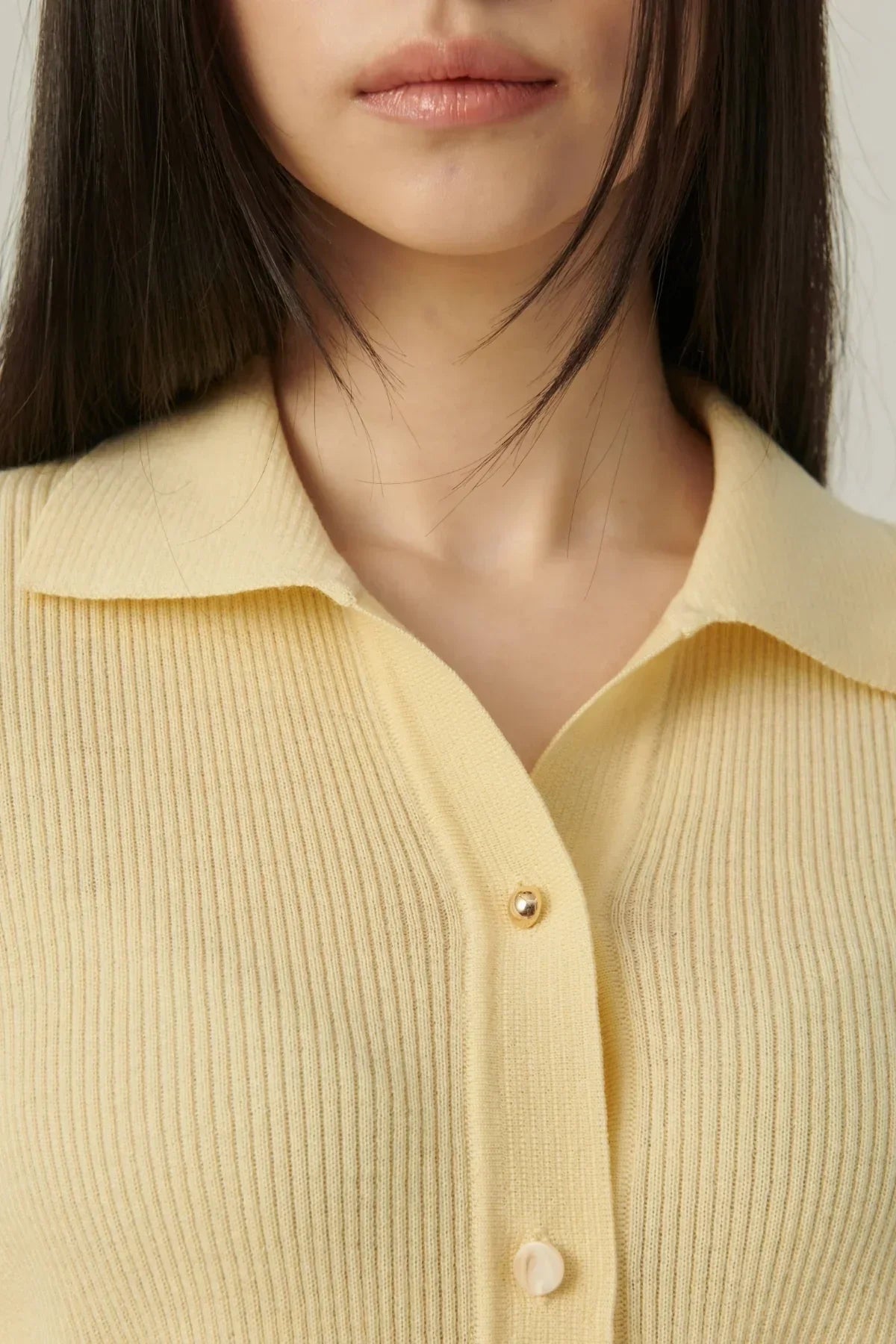 Close-up of a woman wearing a pale yellow collared rib knit cardigan with gold and pearl buttons