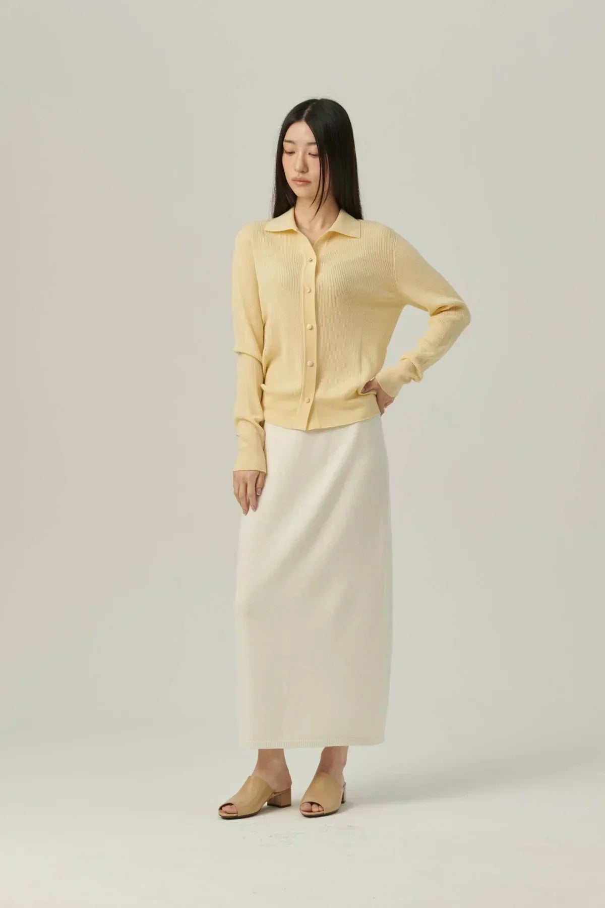 Woman wearing collared yellow rib knit cardigan with long cream skirt and beige open-toe heels