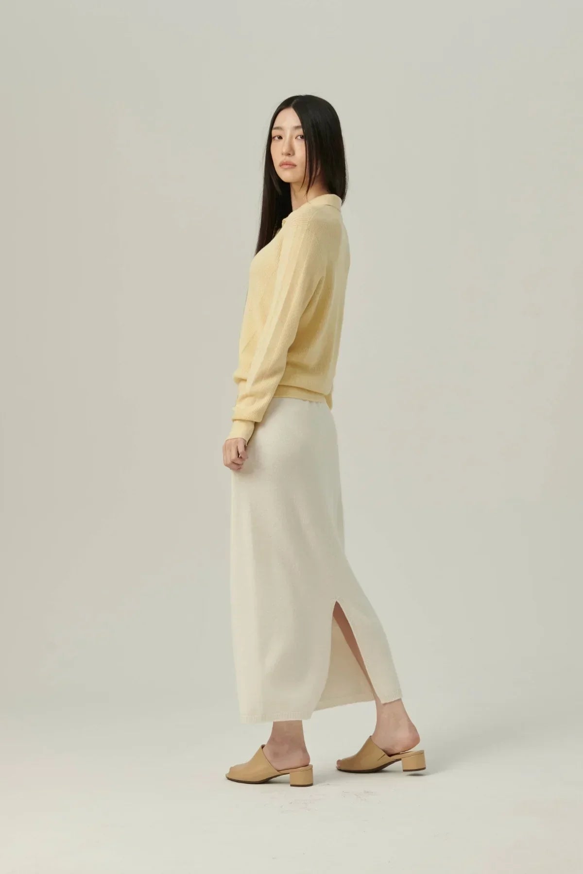 Woman wearing yellow rib knit cardigan and white midi skirt with slit, beige heeled mules