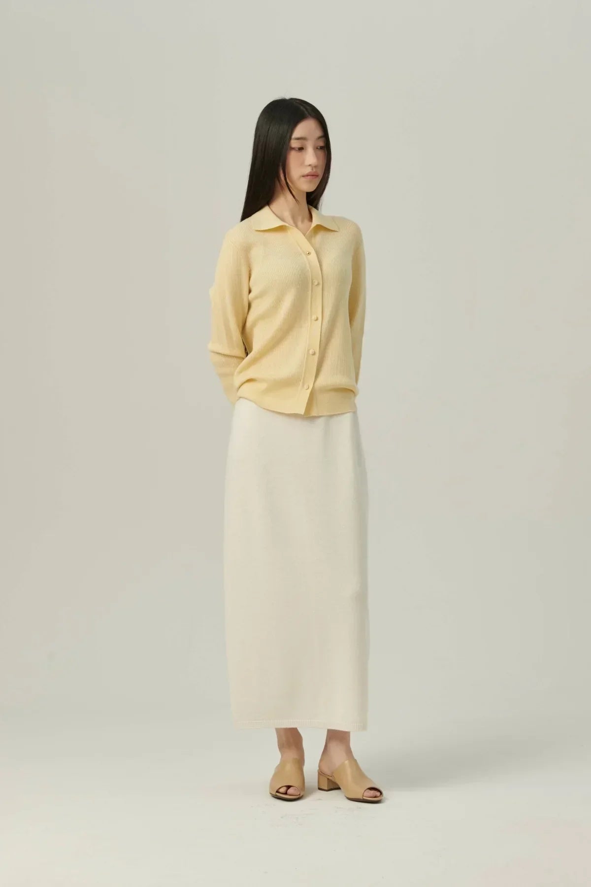 Woman wearing yellow collared rib knit cardigan and white long skirt with beige open-toe shoes