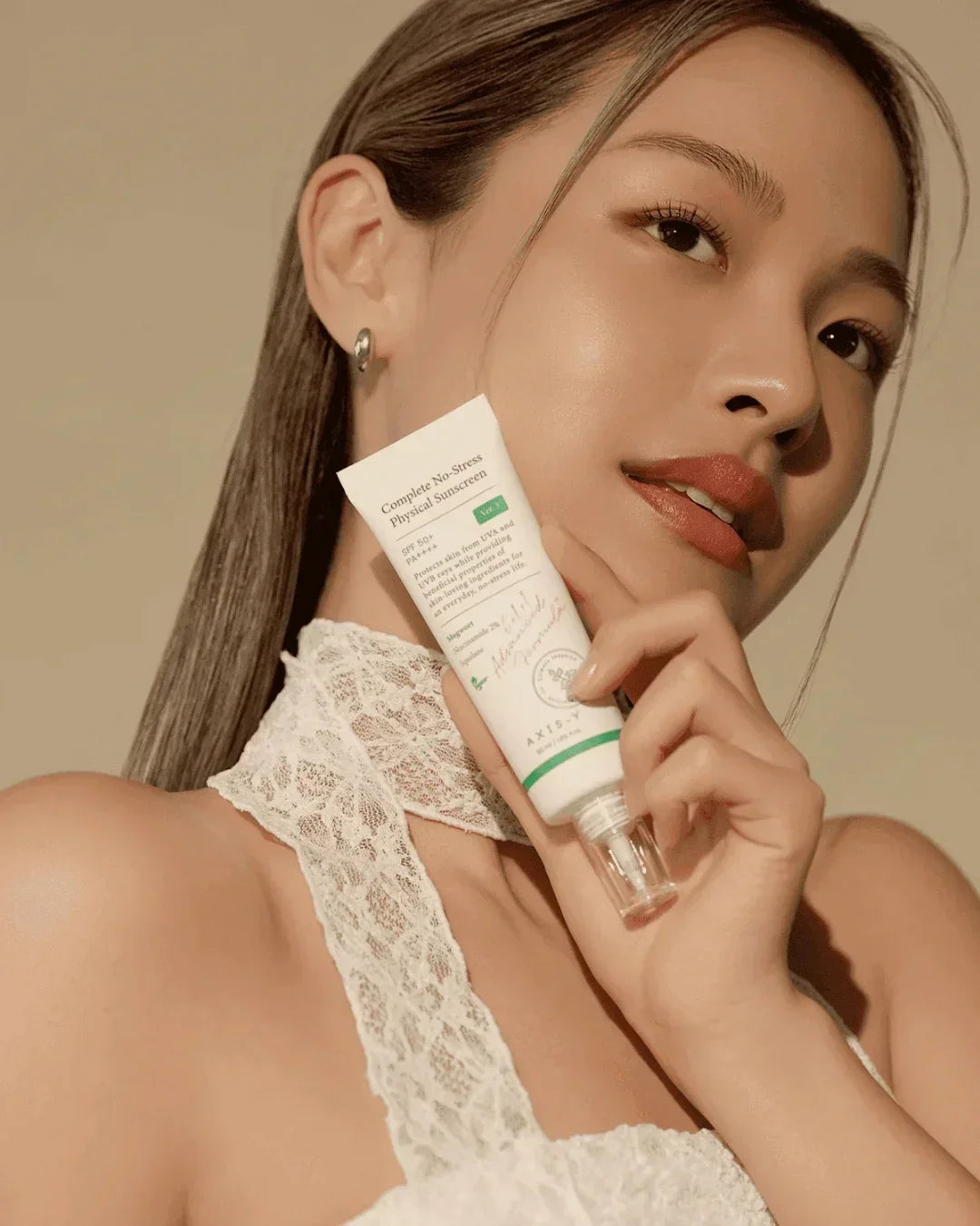 Woman in white lace top holding Complete No-Stress Physical Sunscreen SPF 50+ with clear pump