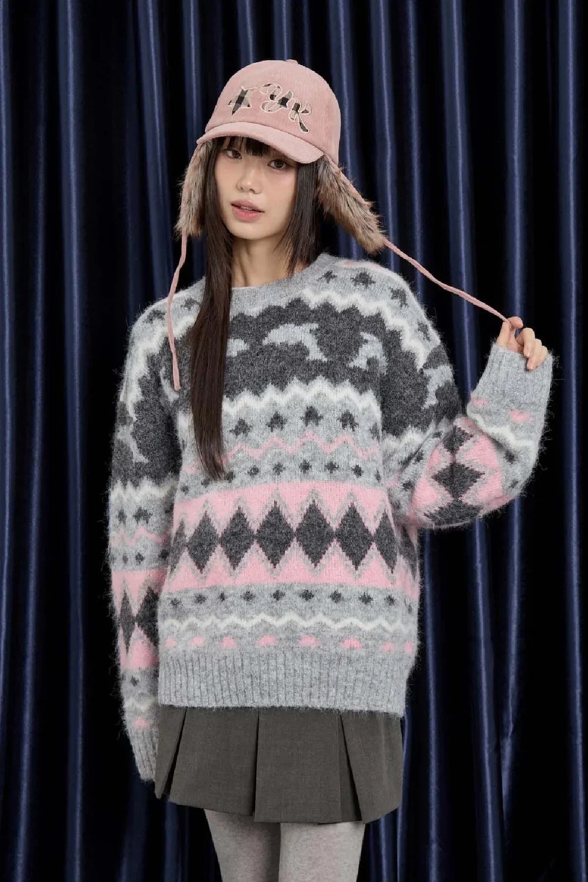 Woman wearing a pink corduroy trooper hat with ear flaps and a patterned grey and pink wool sweater
