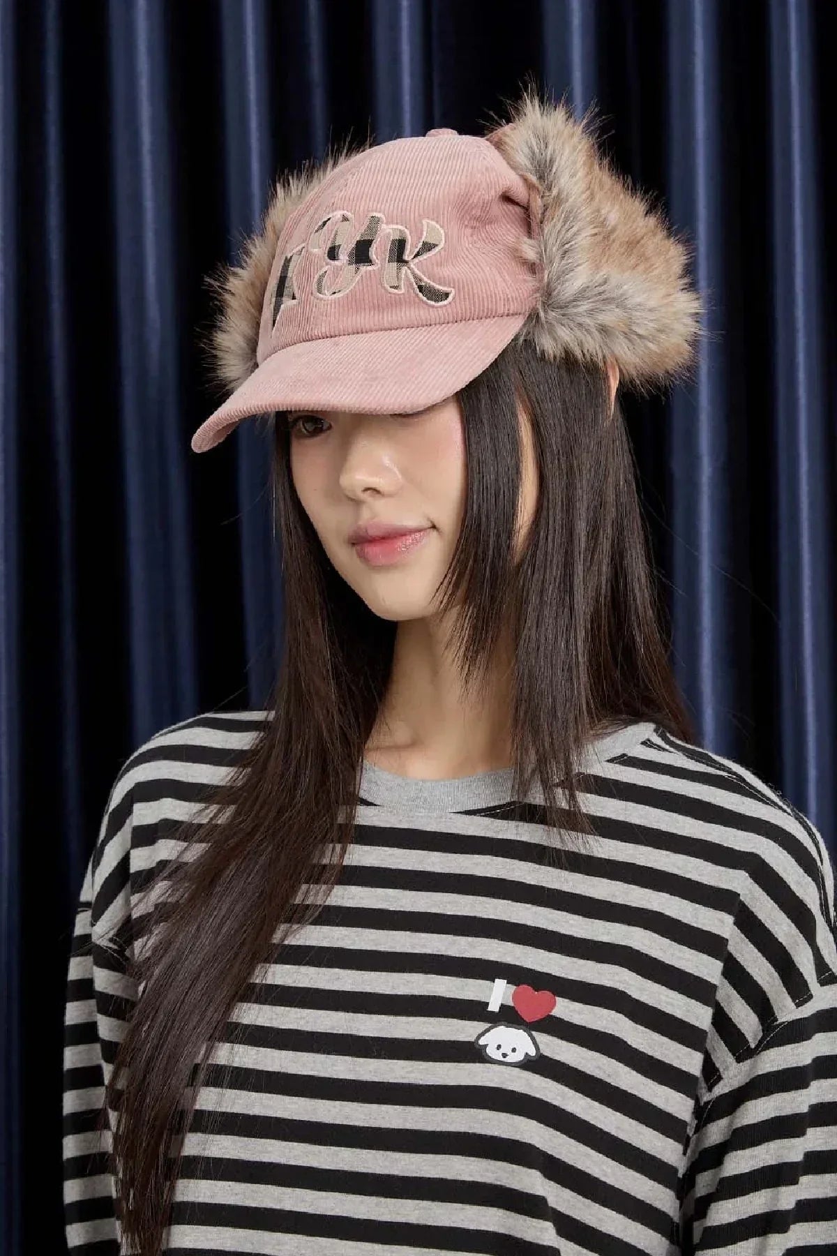 Woman wearing pink corduroy trooper cap with fur ear flaps and striped black and gray shirt