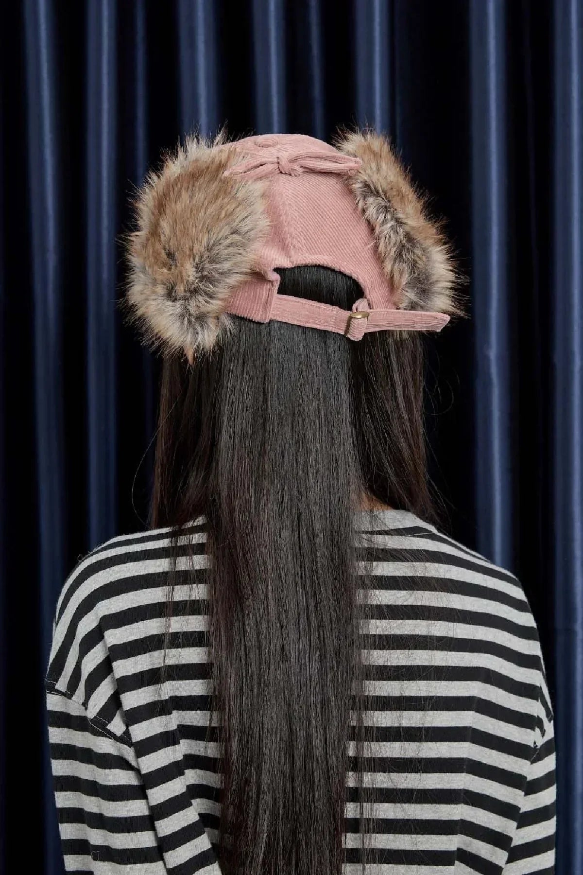 back view of person wearing pink corduroy cap with fur ear flaps and black white striped shirt