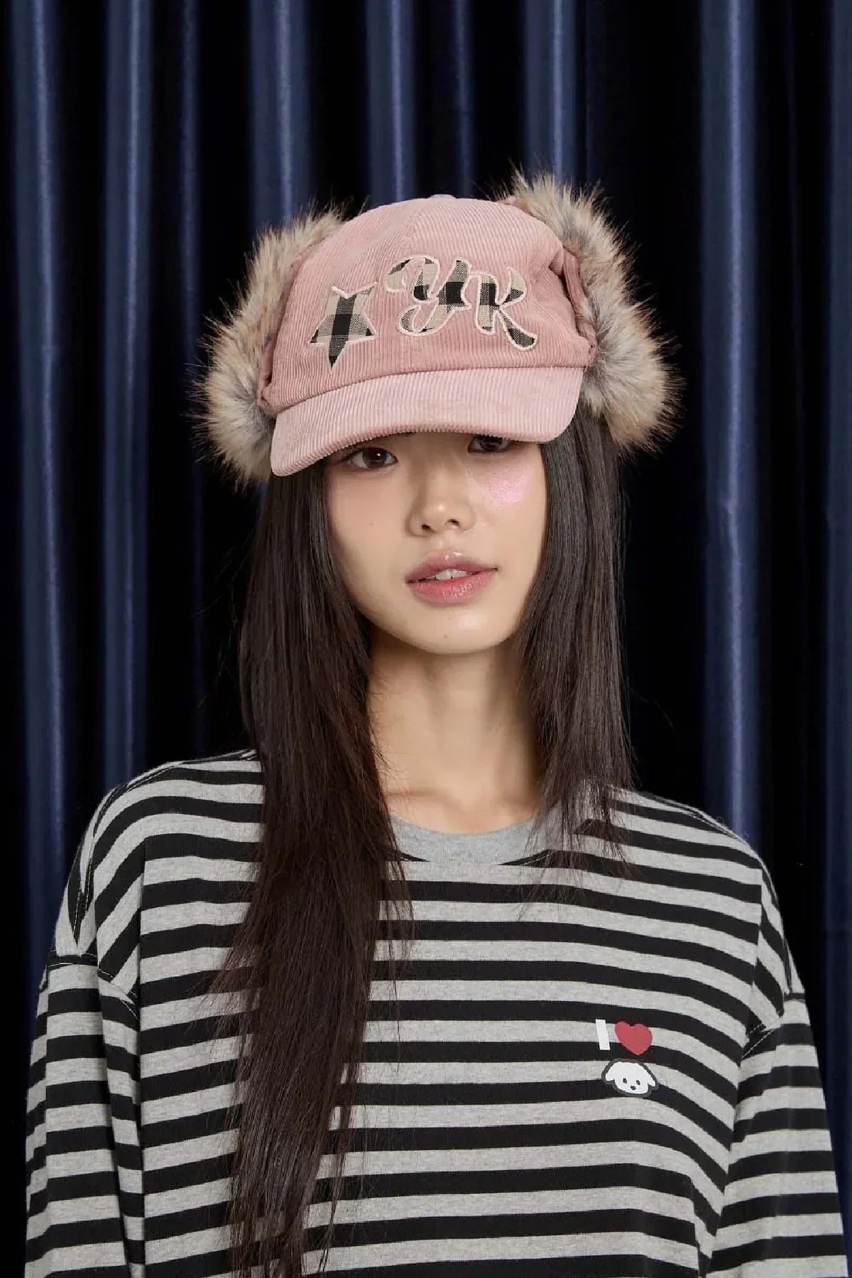 Young woman wearing pink corduroy trooper cap with check applique and faux fur ear flaps, striped shirt