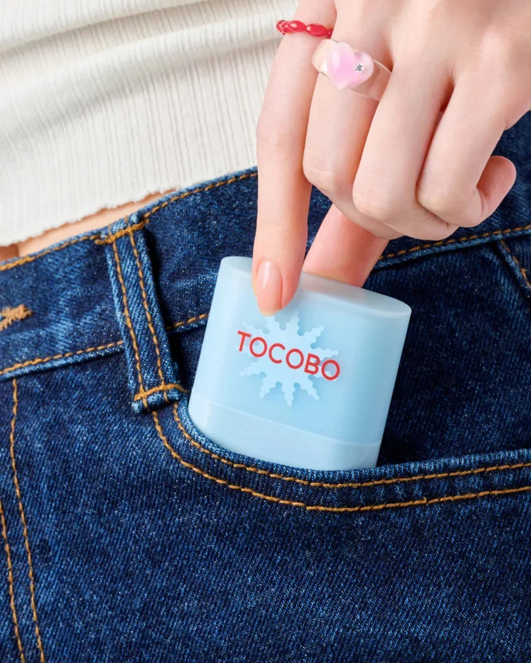 Hand placing blue TOCOBO sunscreen stick into front pocket of blue denim jeans