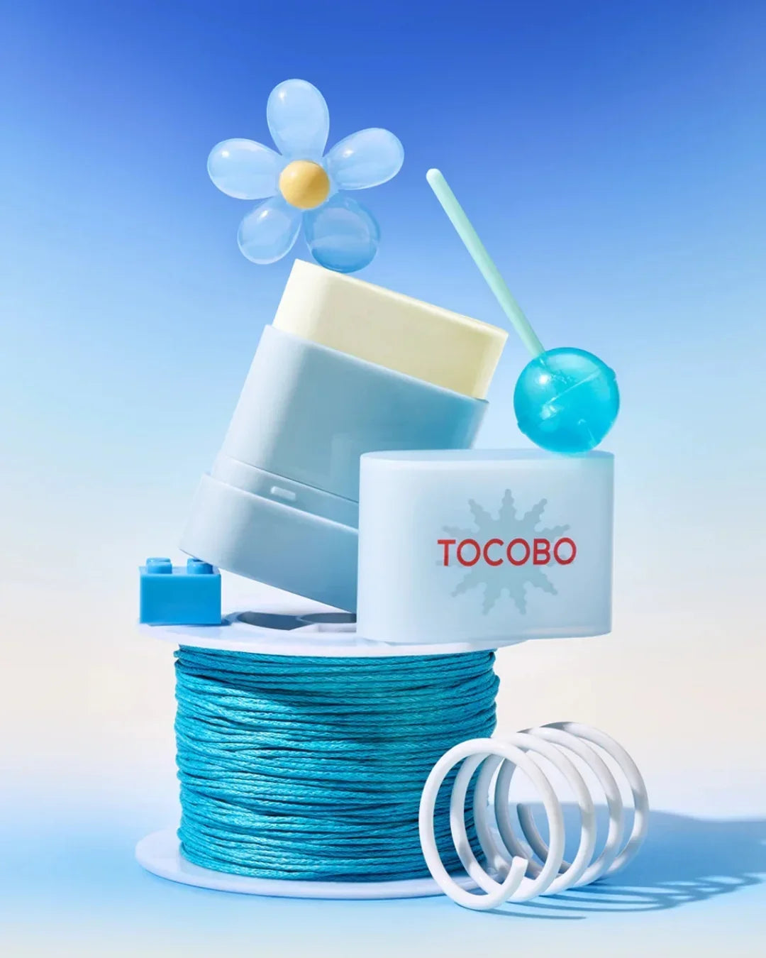 TOCOBO blue sun stick sunscreen with flower decoration and lollipop against blue sky