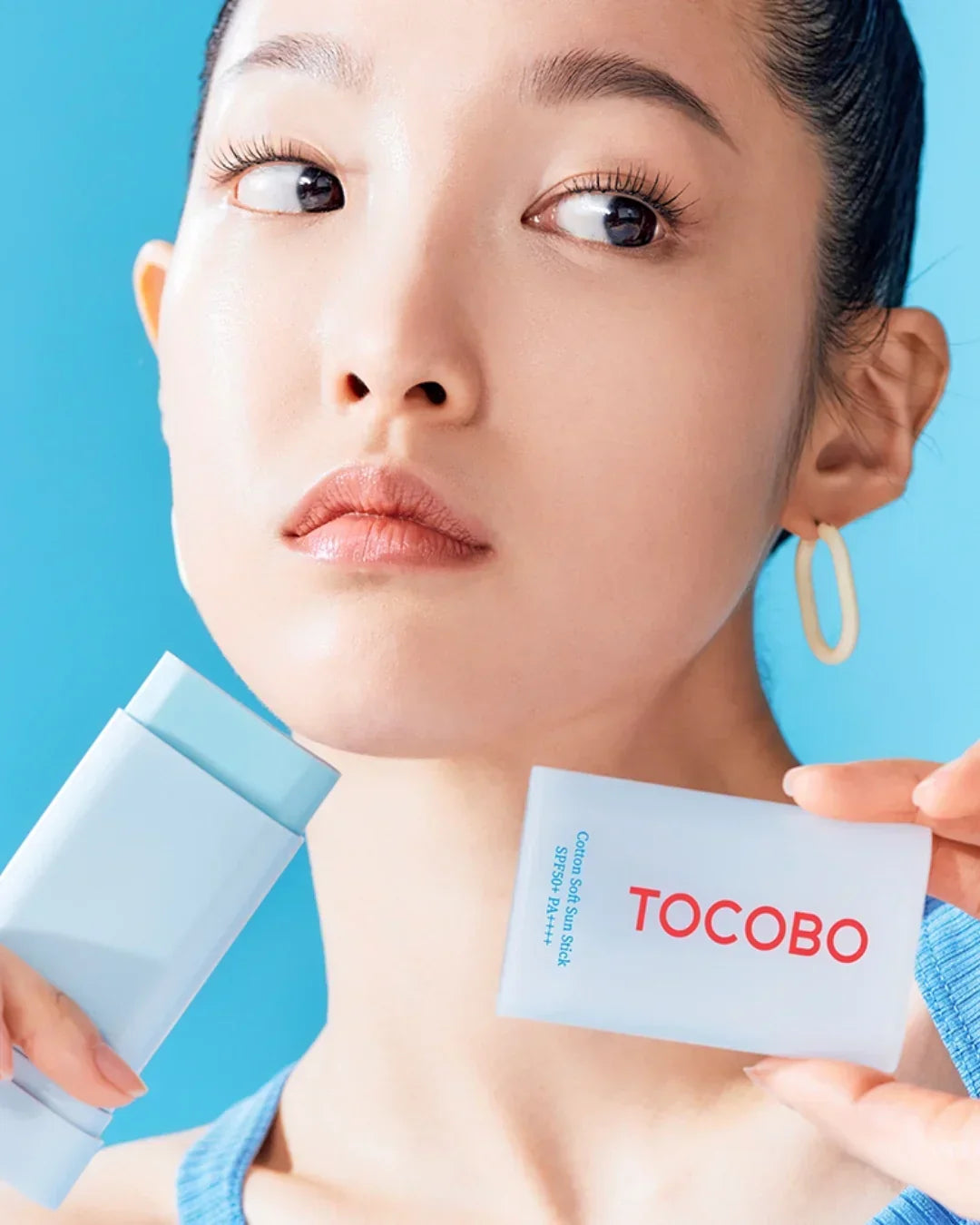 Close-up of woman holding TOCOBO Cotton Soft Sun Stick SPF50 PA++++ with blue background