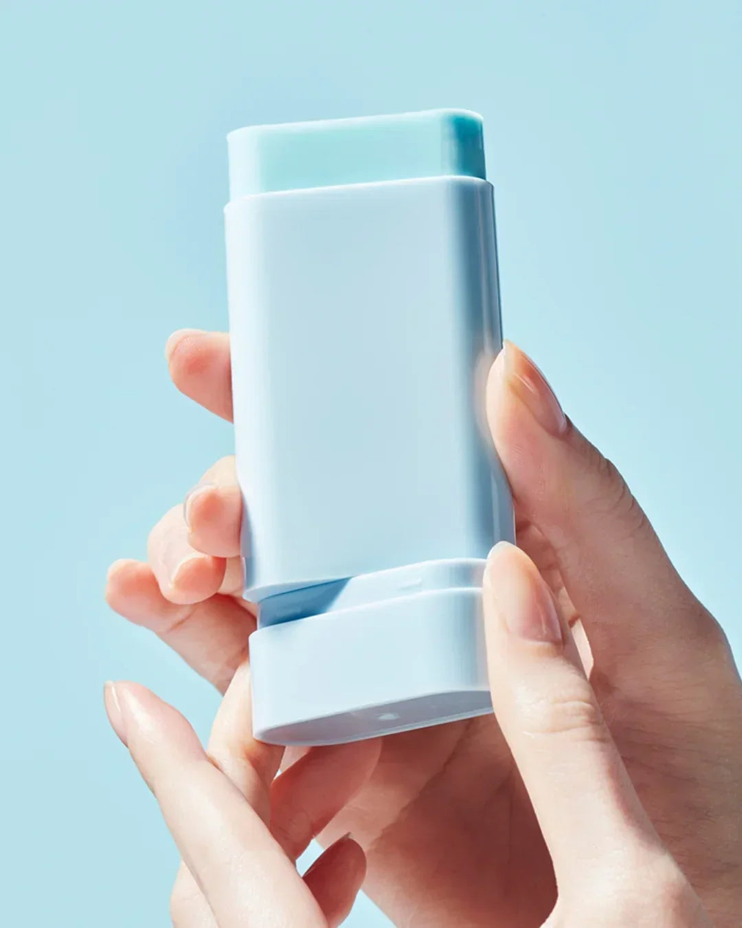 Hand holding light blue sunscreen sun stick with smooth texture against light blue background