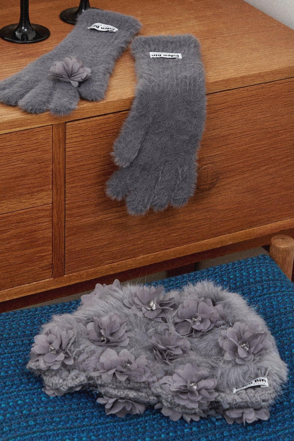 Gray mink fur gloves with flower appliques displayed on wooden cabinet and blue textured surface