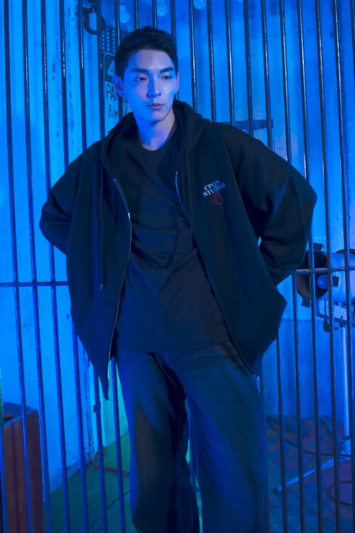 Man wearing black zip-up hoodie with CPGN Studio logo in blue-lit industrial setting