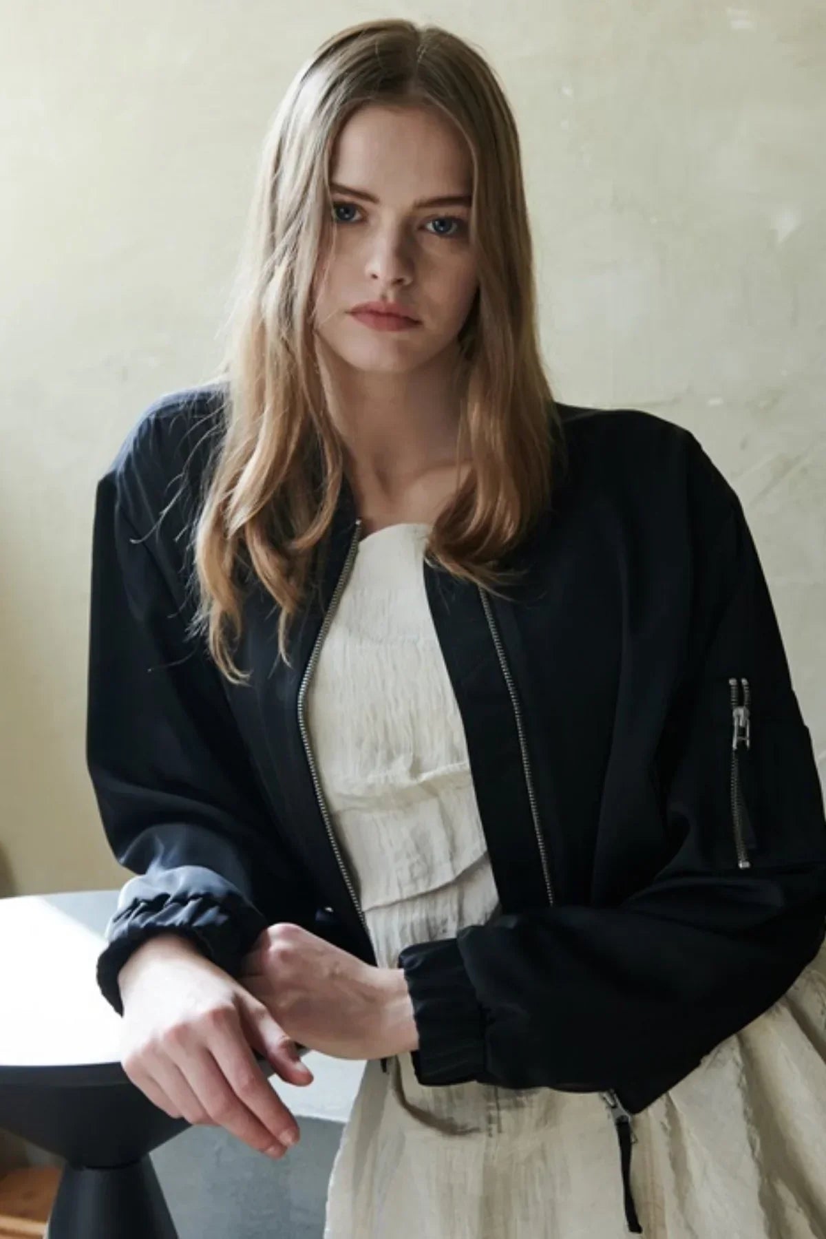 Close-up of woman wearing a black satin bomber jacket over a white textured dress indoors