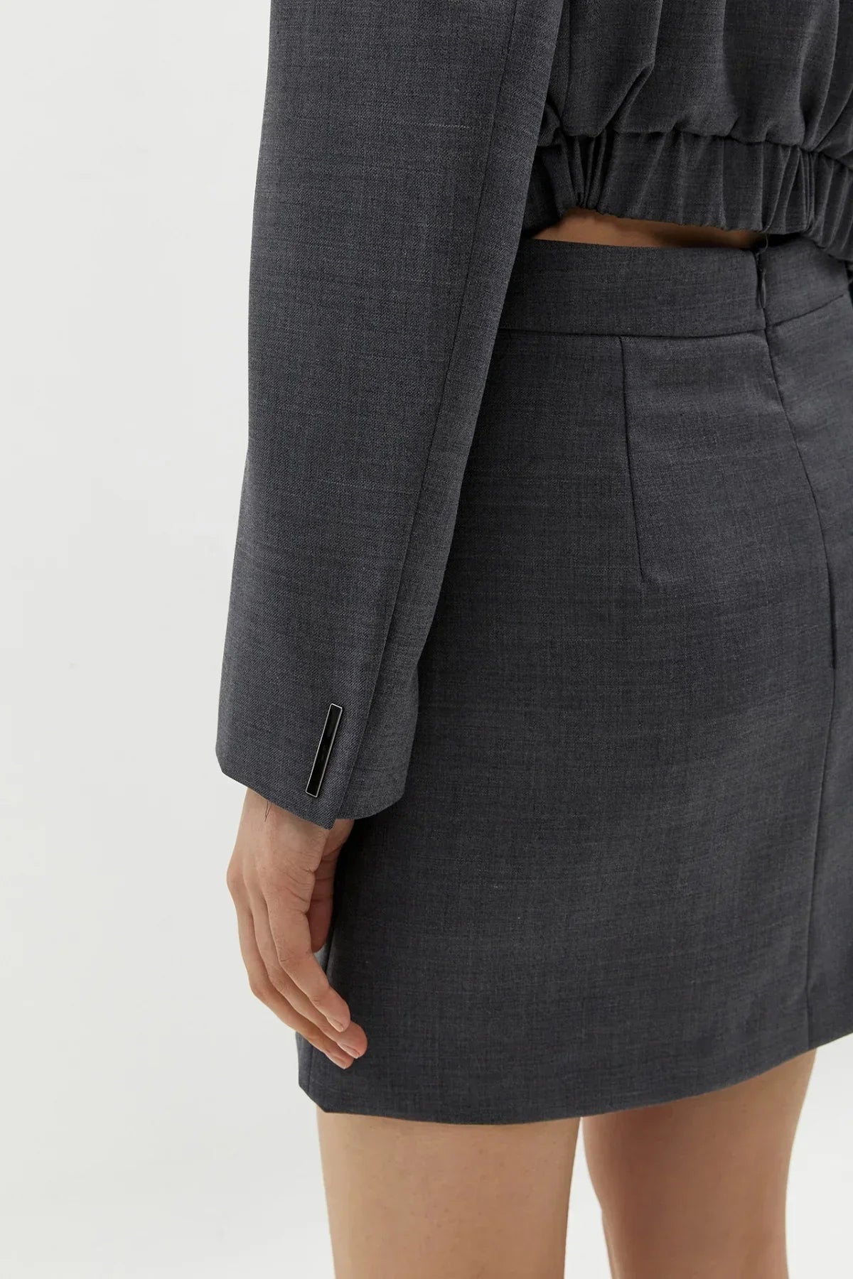 Close-up of a woman wearing a tailored dark grey blazer and matching mini skirt with textured fabric
