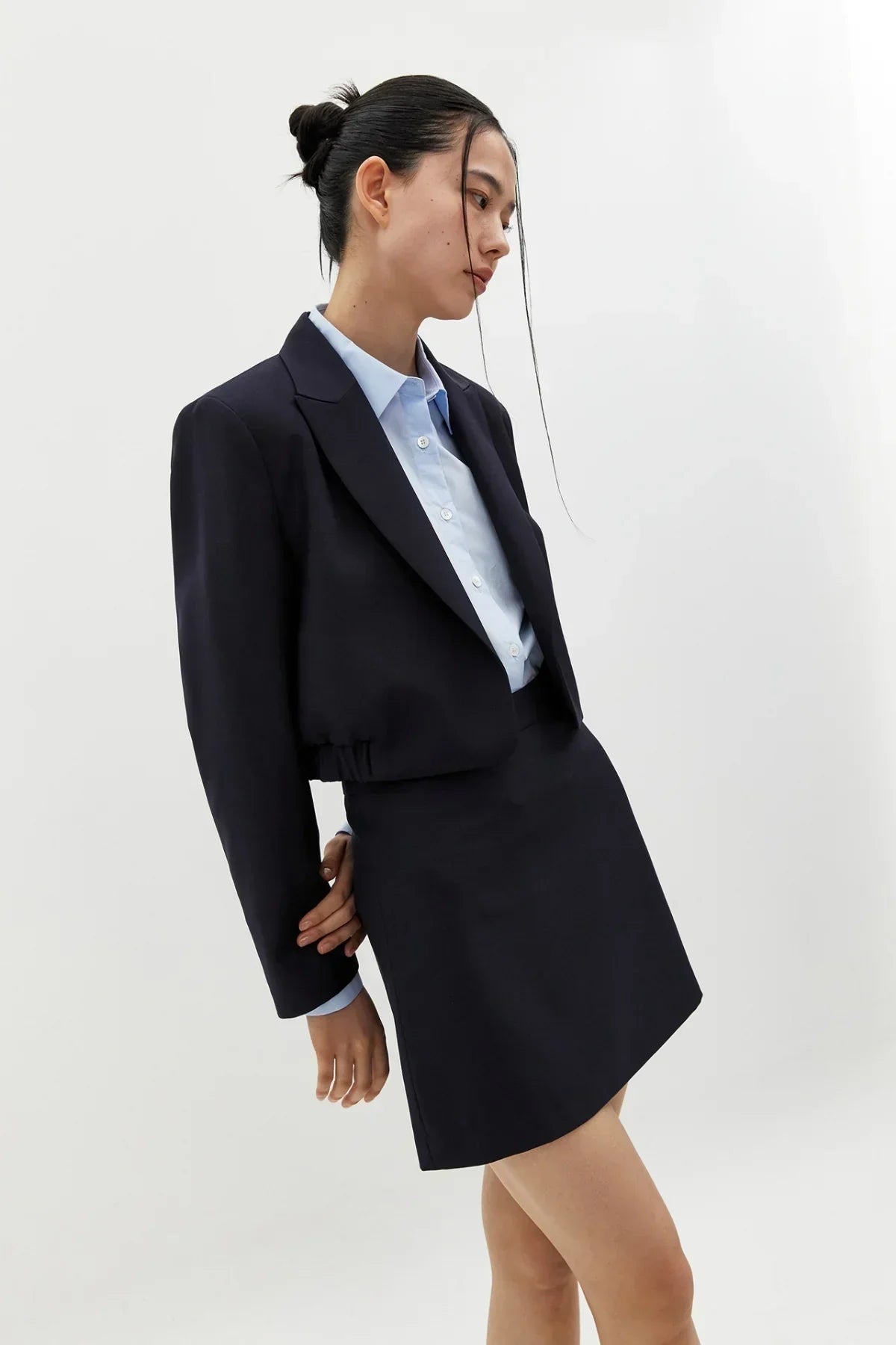 Woman wearing navy cropped blazer and matching skirt over light blue button-up shirt in studio