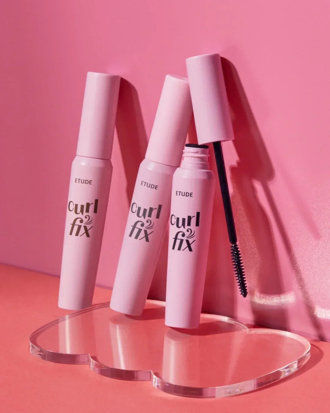 Etude Curl Fix mascara tubes in pink packaging on heart-shaped clear stand with pink backdrop