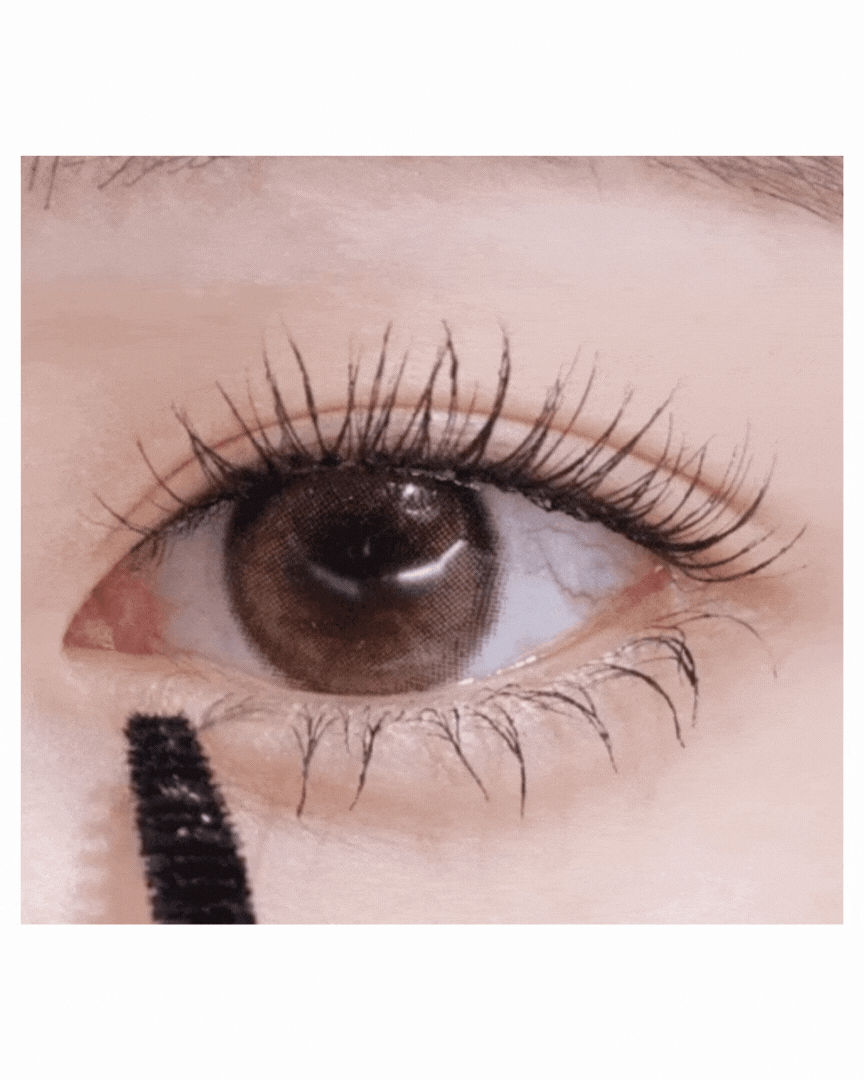 Close-up of brown eye with long curled eyelashes applying black mascara