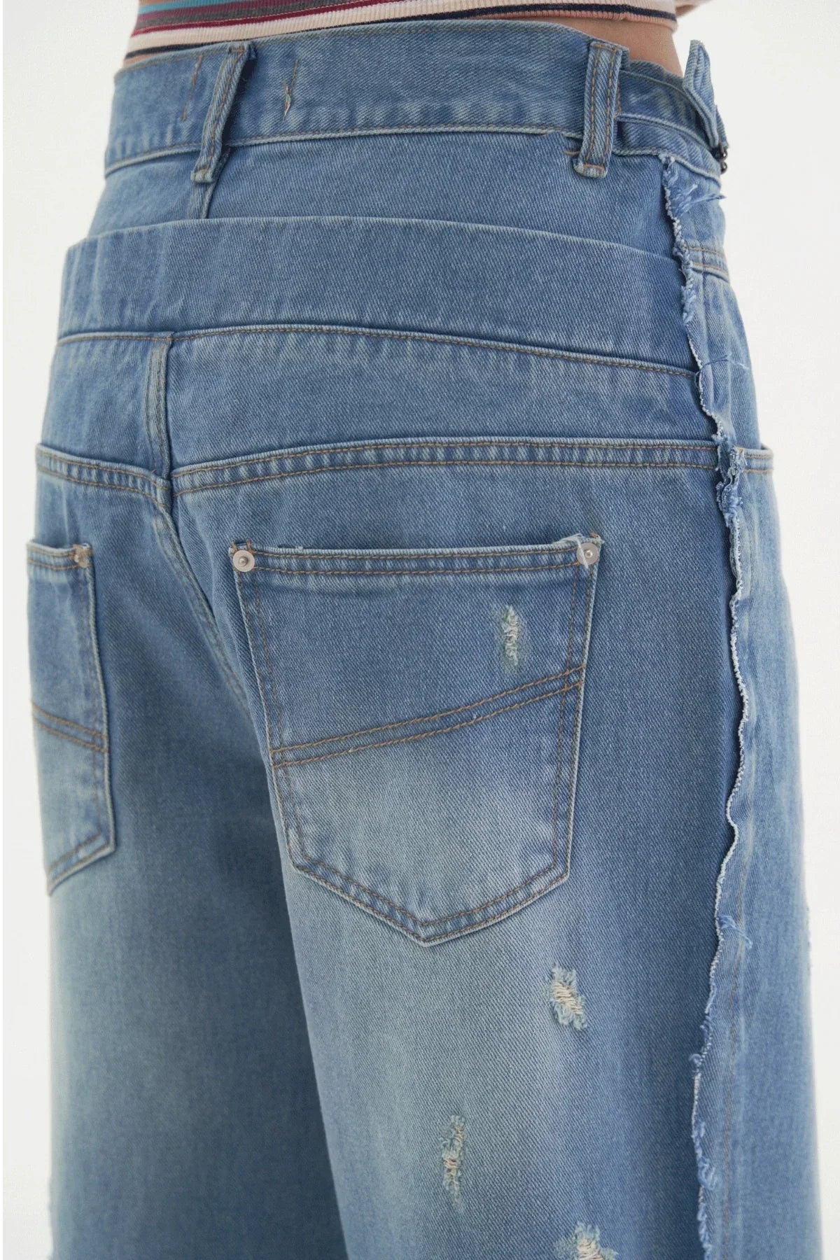 Close-up of blue denim wide-leg pants with frayed raw hem and distressed details