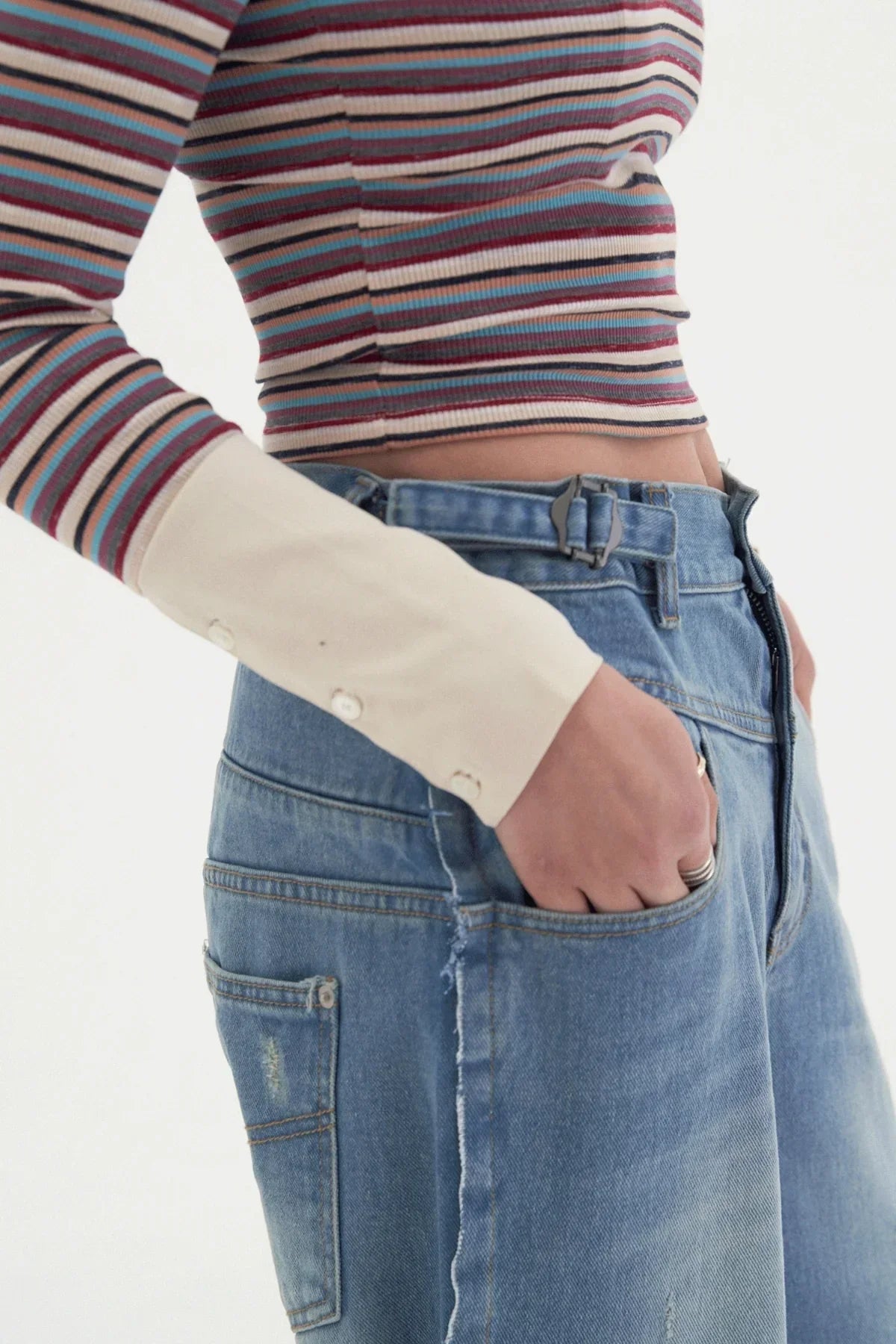 Close-up of person wearing wide blue denim jeans with belt and striped long sleeve crop top
