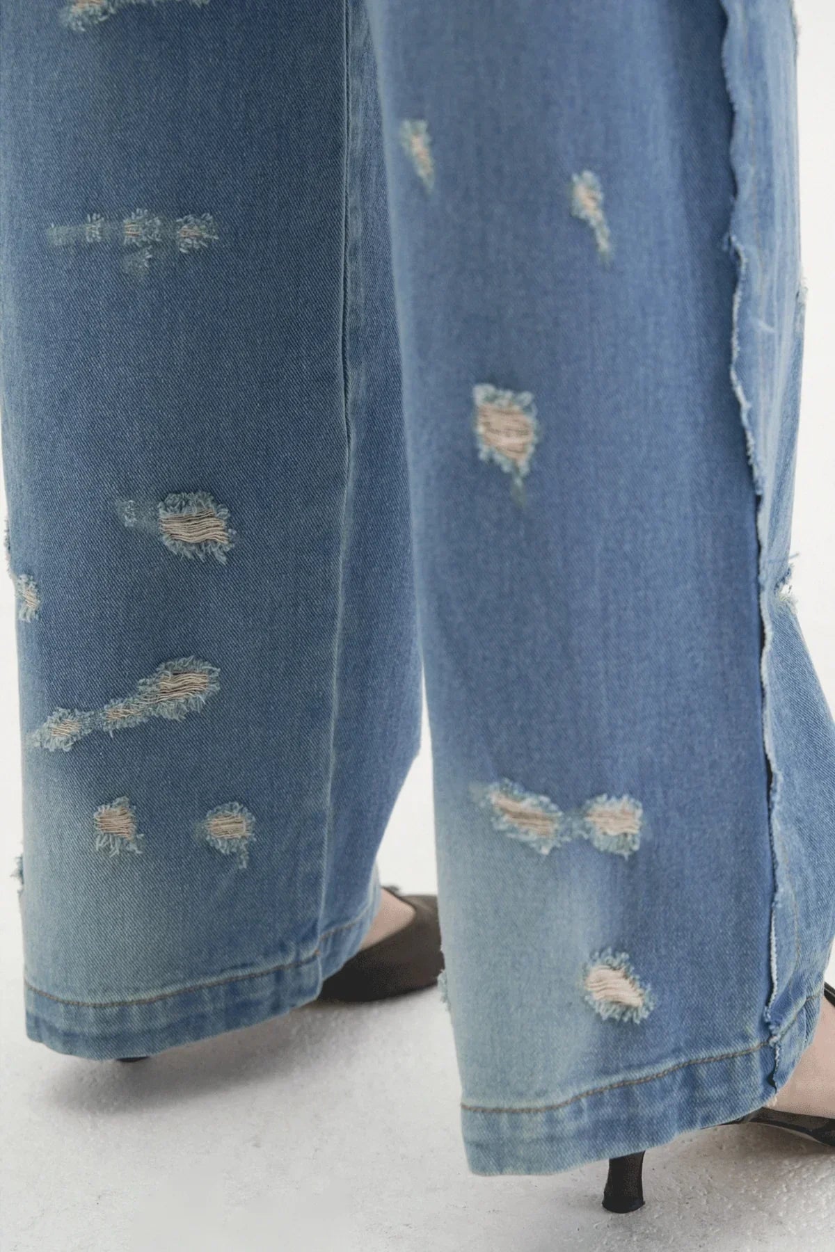 Close-up of light blue wide-leg distressed denim jeans with frayed patches and split hems