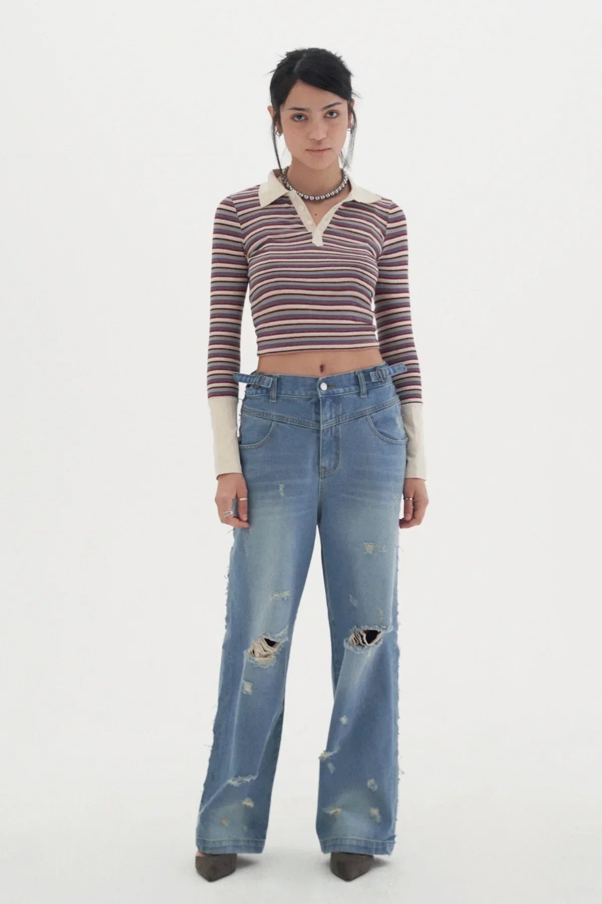 woman in striped long-sleeve crop top and distressed wide-leg jeans on white background