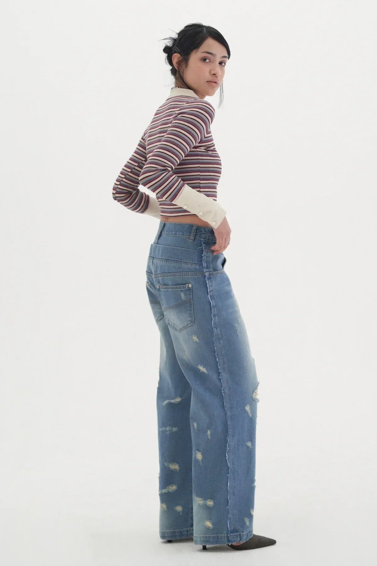 Woman in striped cropped top and distressed wide-leg denim jeans posing against white background