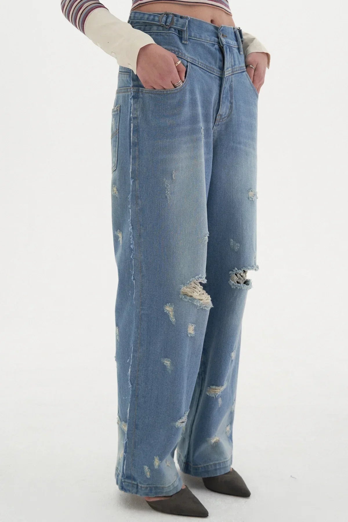 Close-up of person wearing ripped wide-leg blue denim jeans with pockets, paired with striped top and pointed shoes