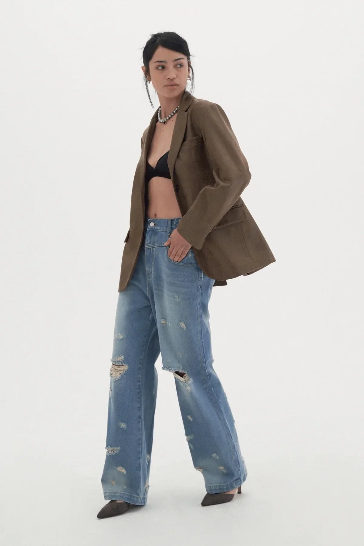 Model wearing oversized brown blazer, black bralette, distressed wide-leg jeans, and pointed heels