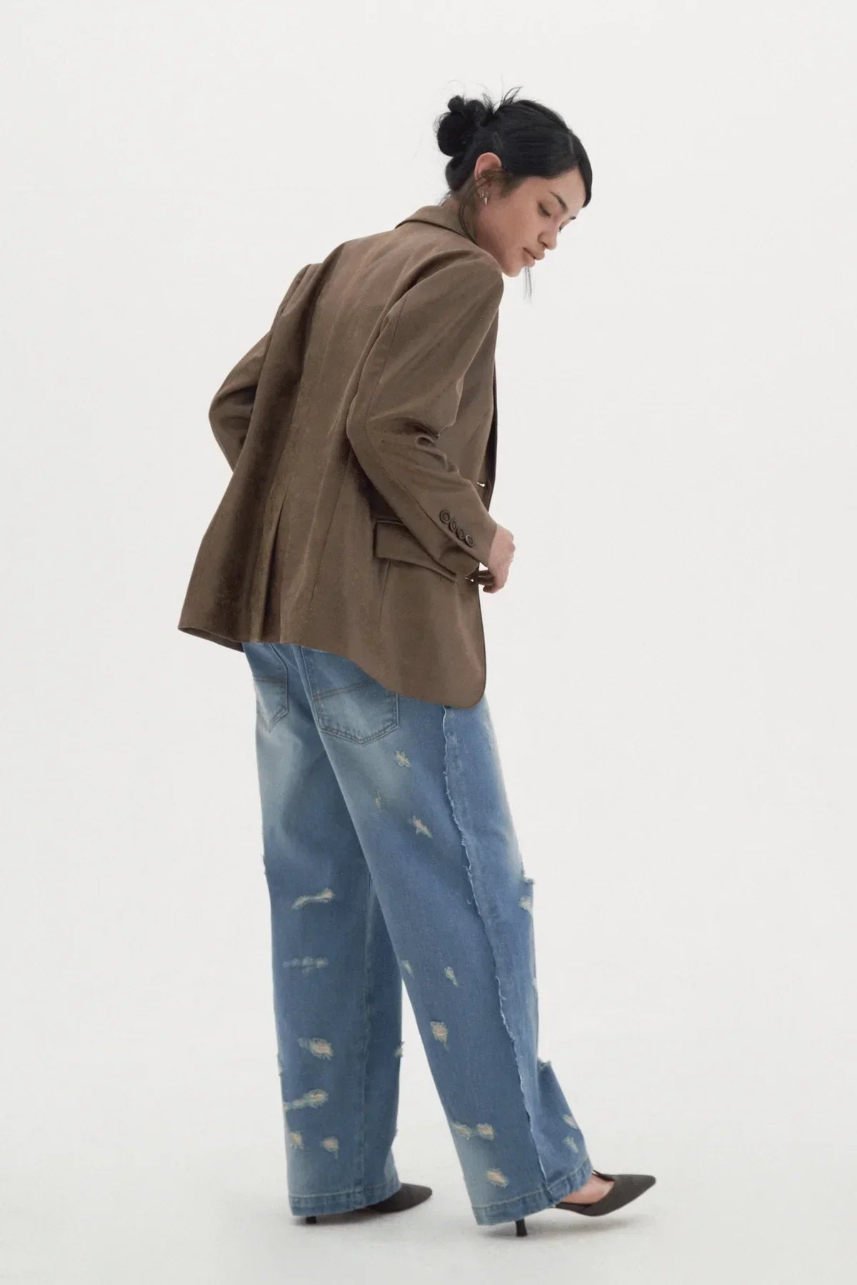 Woman in distressed wide-leg jeans and brown blazer posing against white background