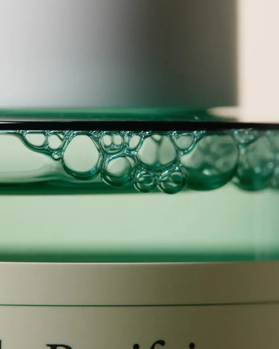 Close-up of green liquid with bubbles on white cosmetic bottle edge in soft lighting
