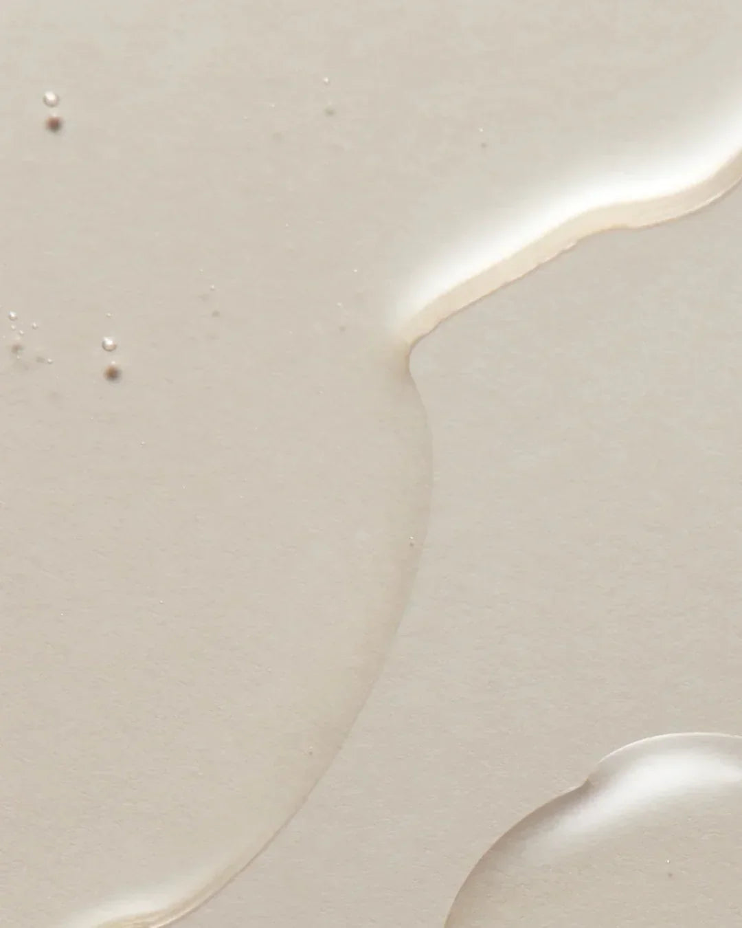 Close-up of clear liquid texture on beige surface, highlighting smooth, glossy skincare product detail