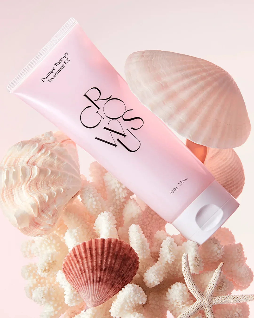 Pink tube of damage therapy hair treatment surrounded by white coral and seashells with starfish