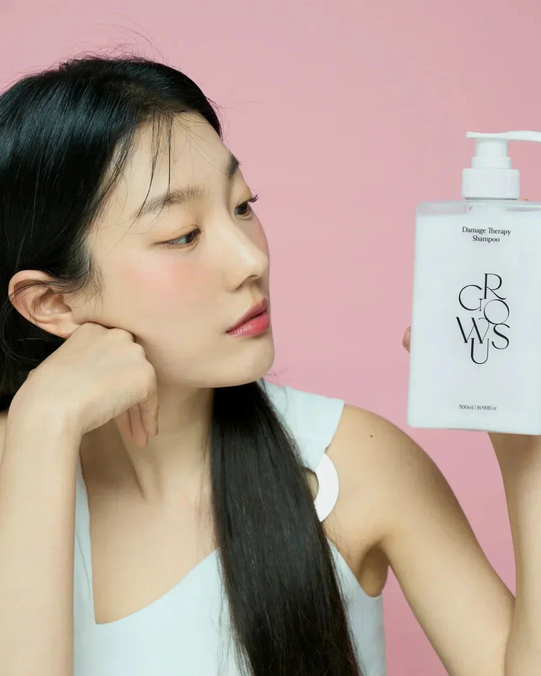Woman with long black hair holding white 500ml Damage Therapy Shampoo bottle against pink background