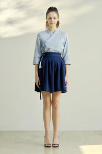 Woman wearing light blue wrap blouse and navy blue pleated mini skirt with tassel accessory