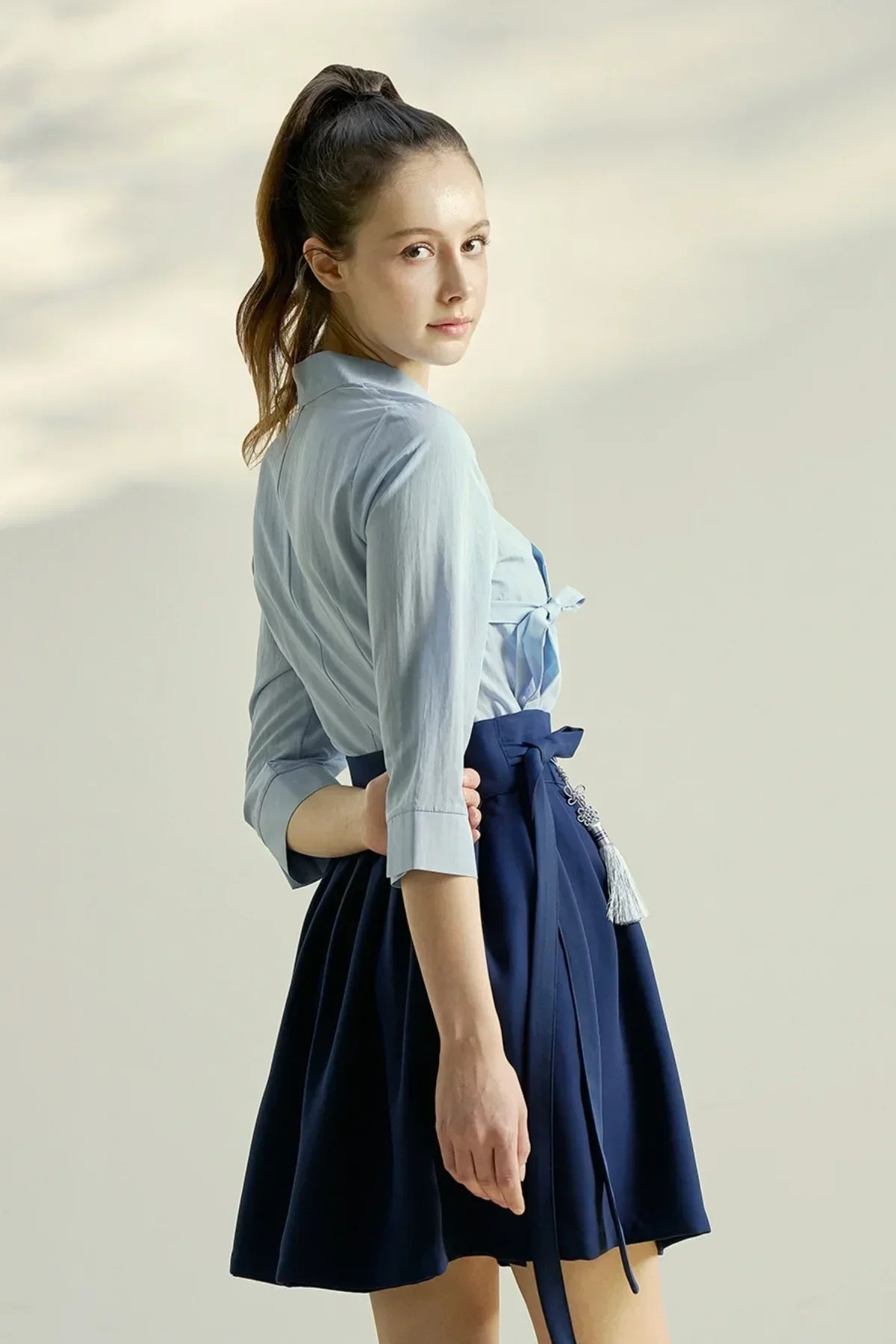 Young woman in a blue blouse and navy mini skirt with a tied waist tassel accessory in studio