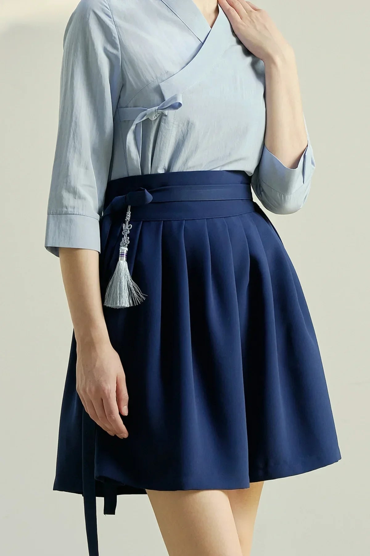 Woman wearing a navy blue pleated mini skirt with a tassel accessory and light blue wrap top