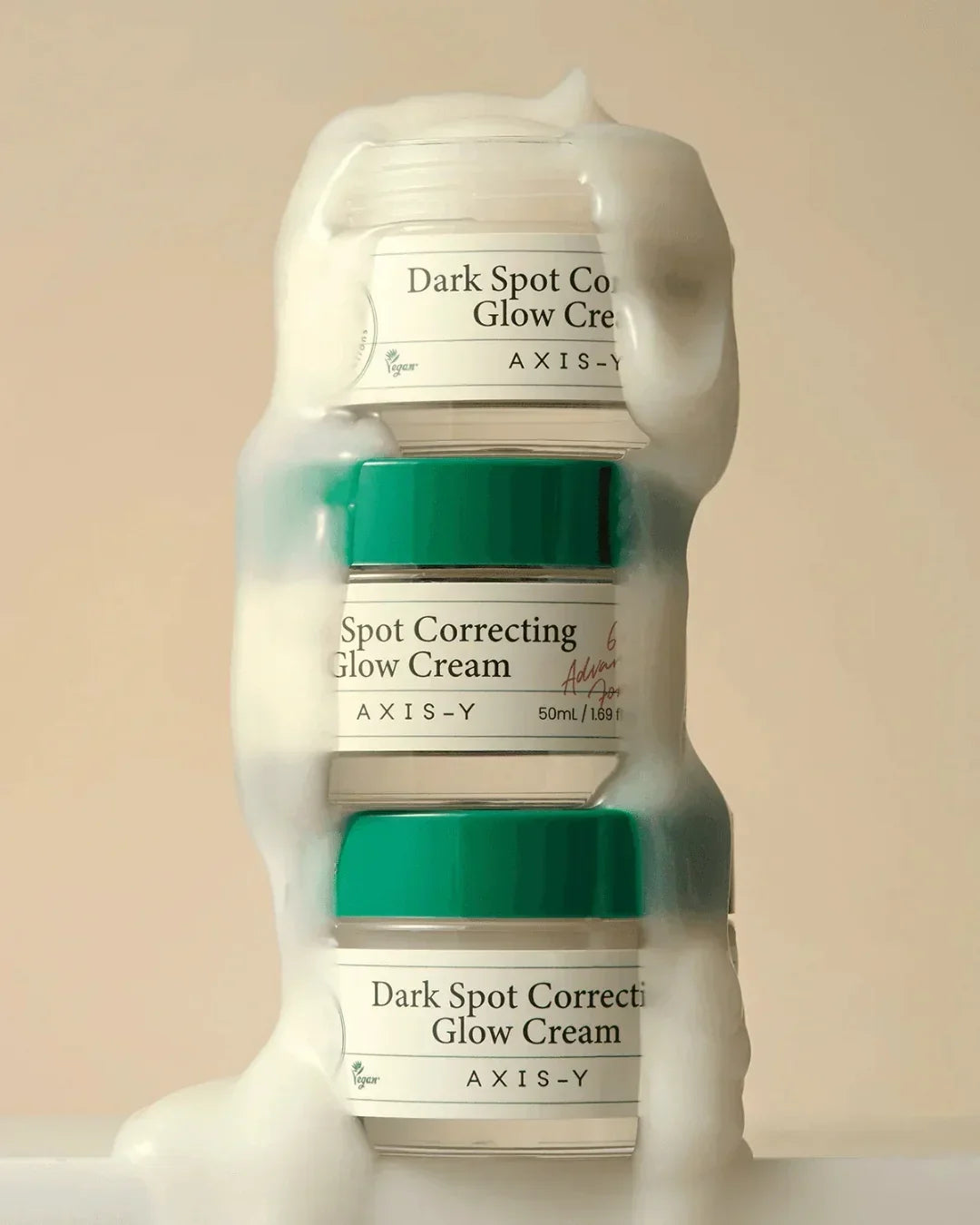 Stack of Axis-Y Dark Spot Correcting Glow Cream jars with cream on beige background