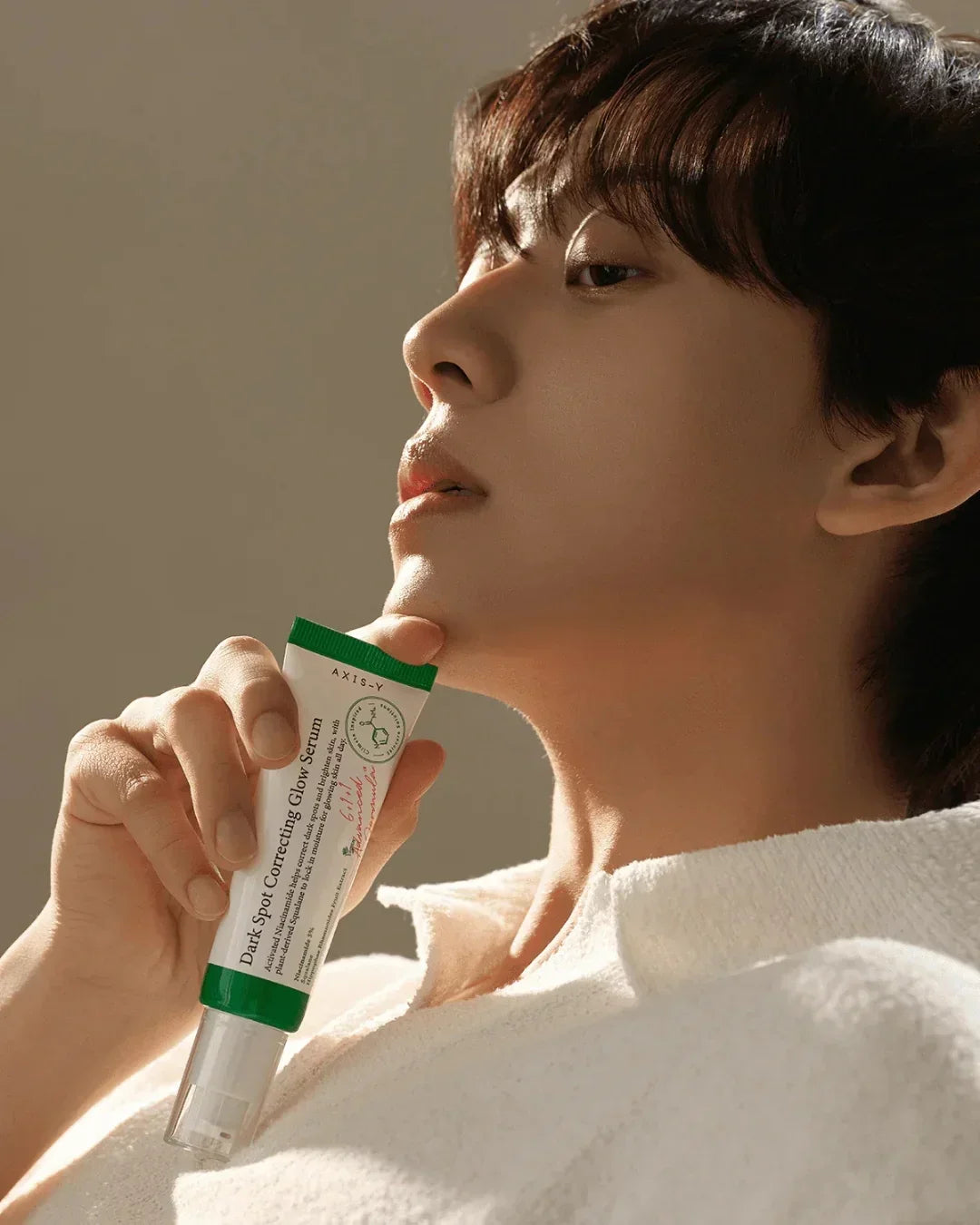 Close-up of person holding Axis-Y Dark Spot Correcting Glow Serum in green and white tube