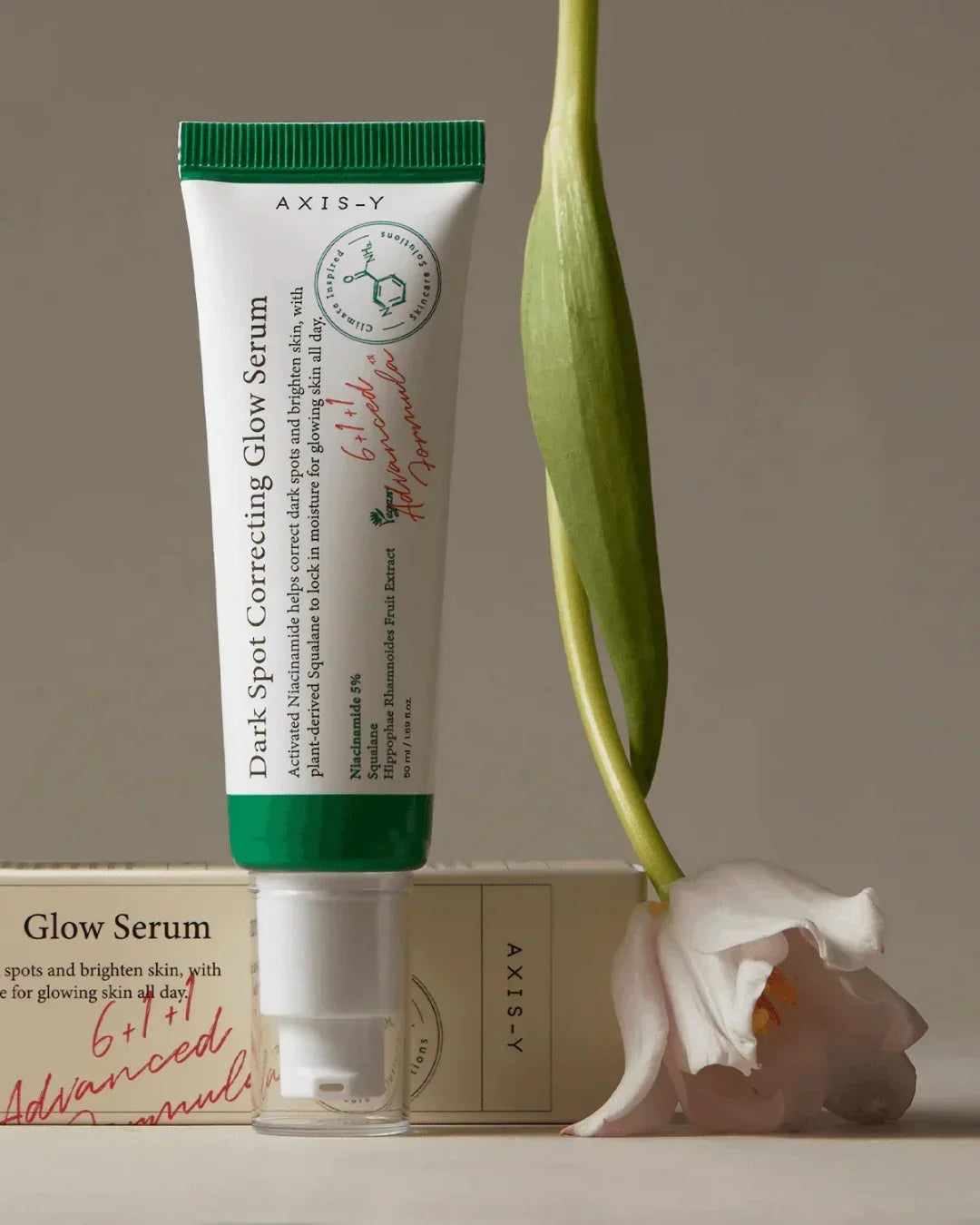 Axis-Y Dark Spot Correcting Glow Serum tube with packaging and a white flower on beige background