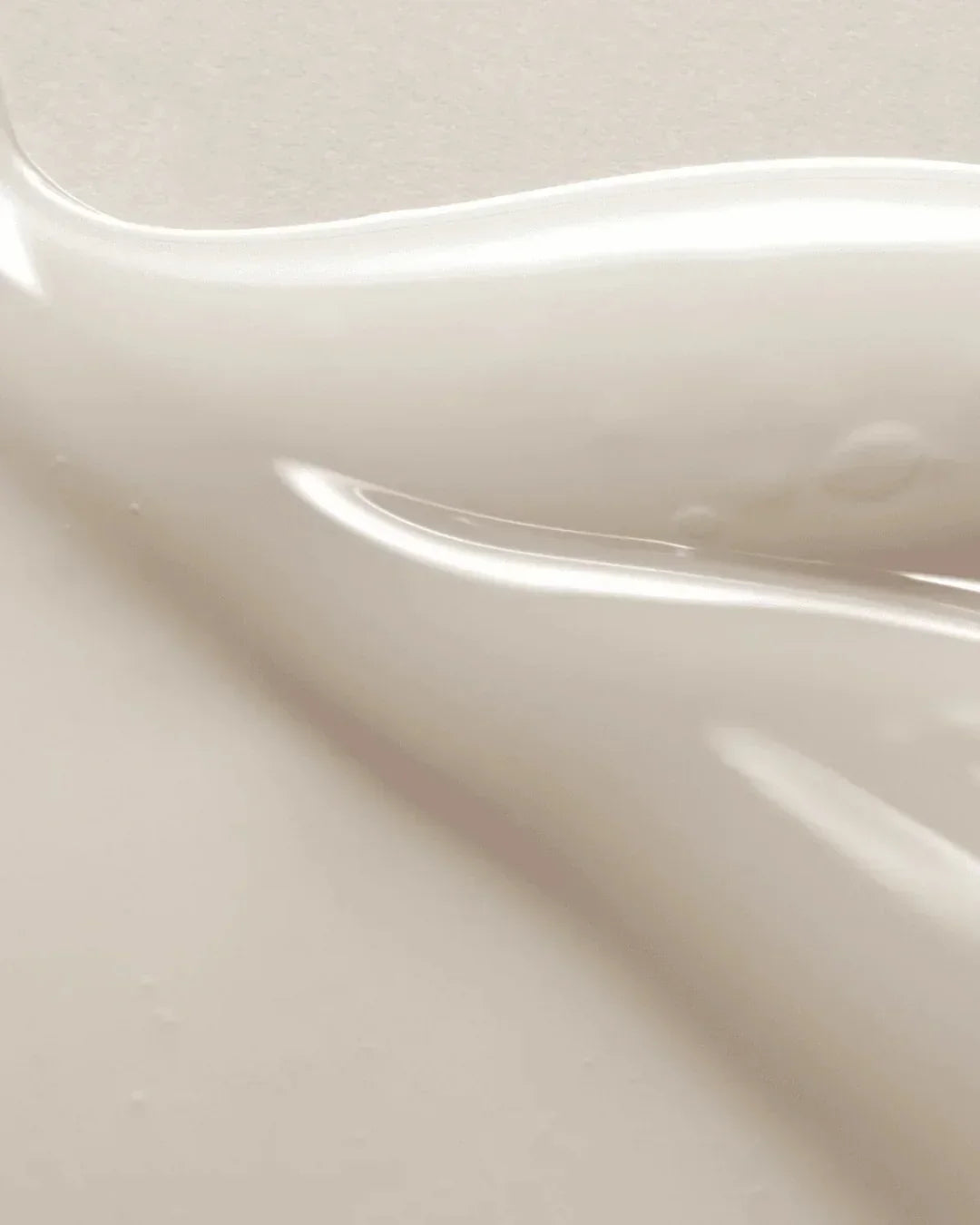 Close-up of creamy beige serum texture with smooth, glossy finish and subtle bubbles